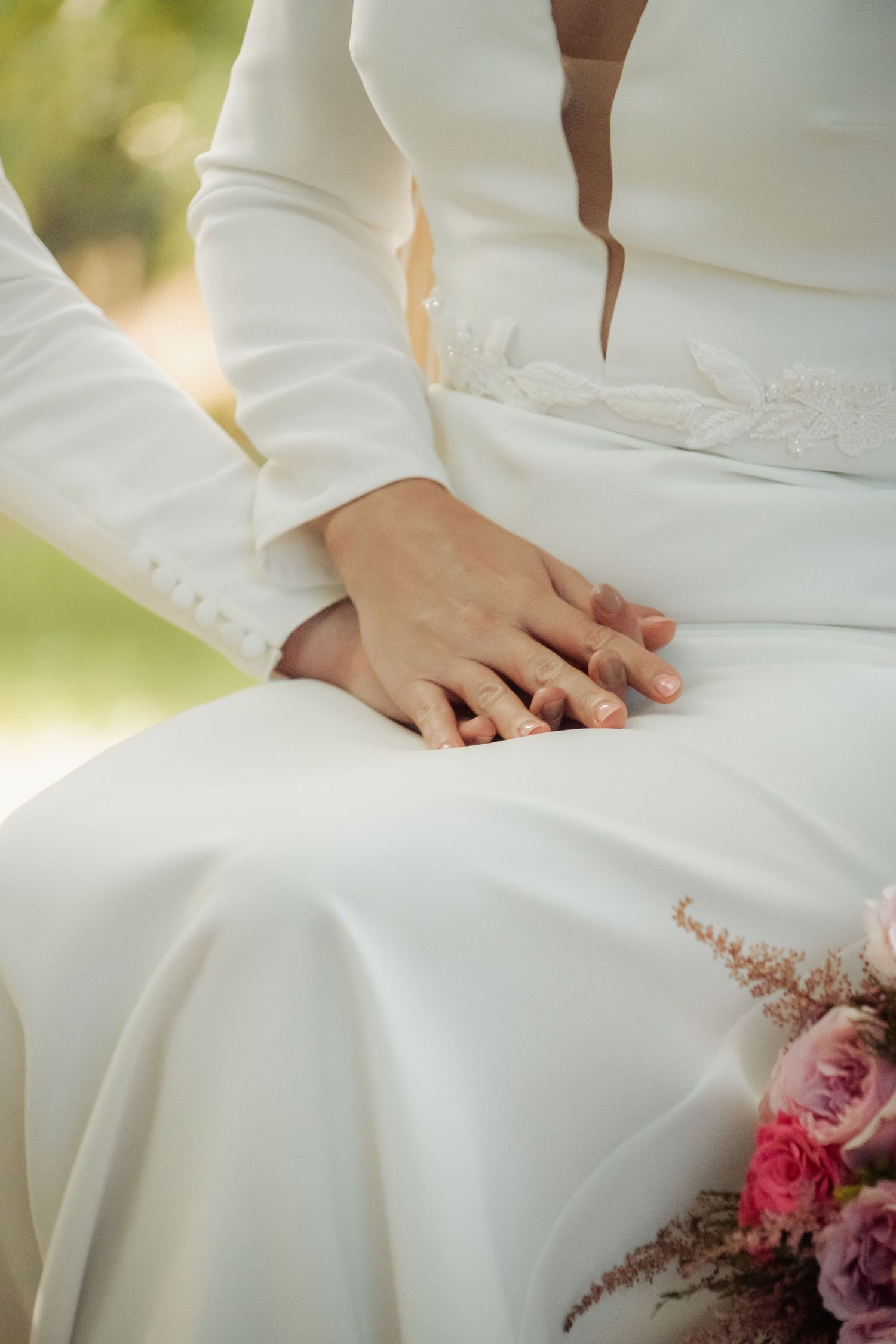 Close-up of bride and groom holding hands during wedding ceremony with floral bouquet.