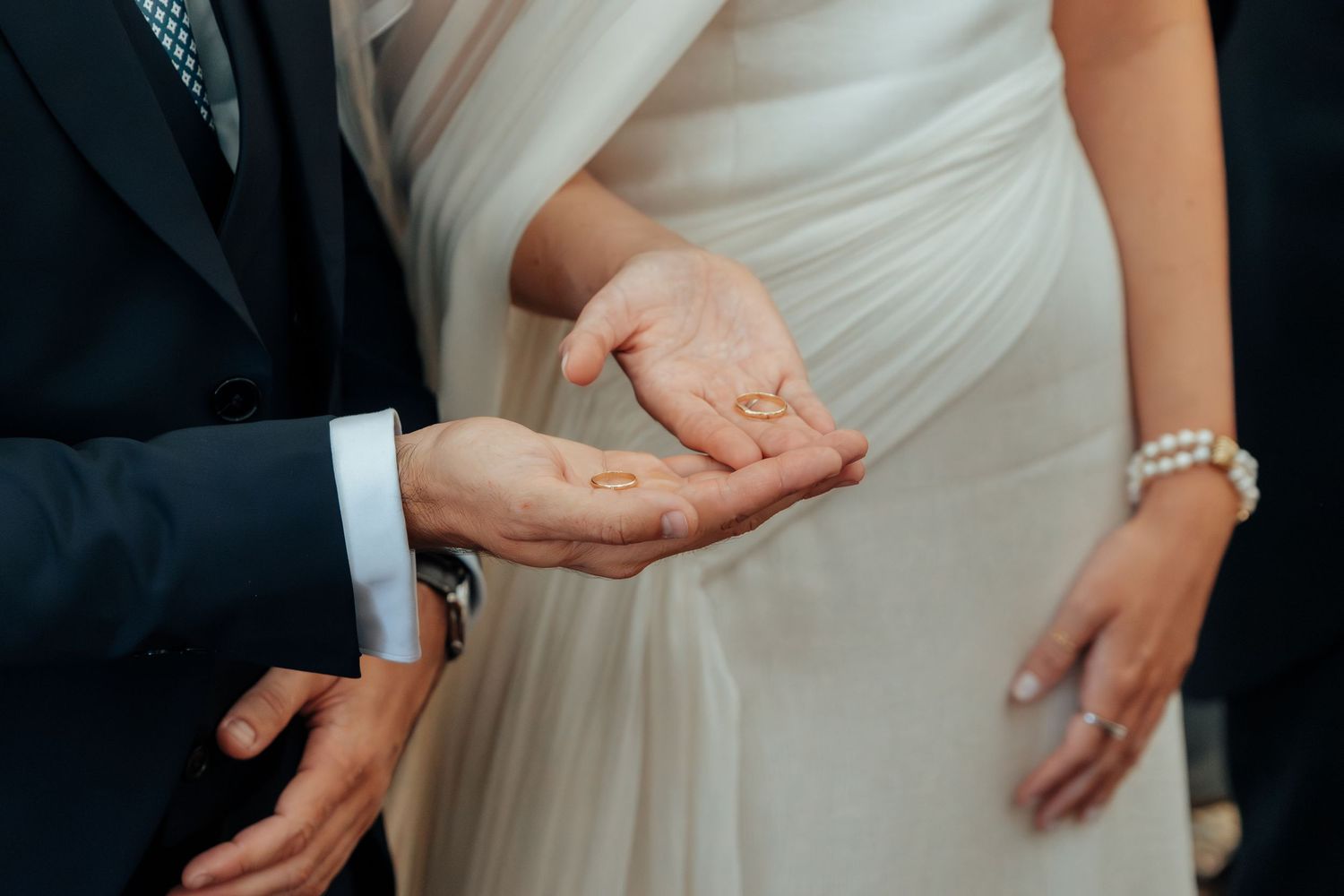 Bride and groom holding gold wedding rings in their open palms during ring exchange ceremony.
