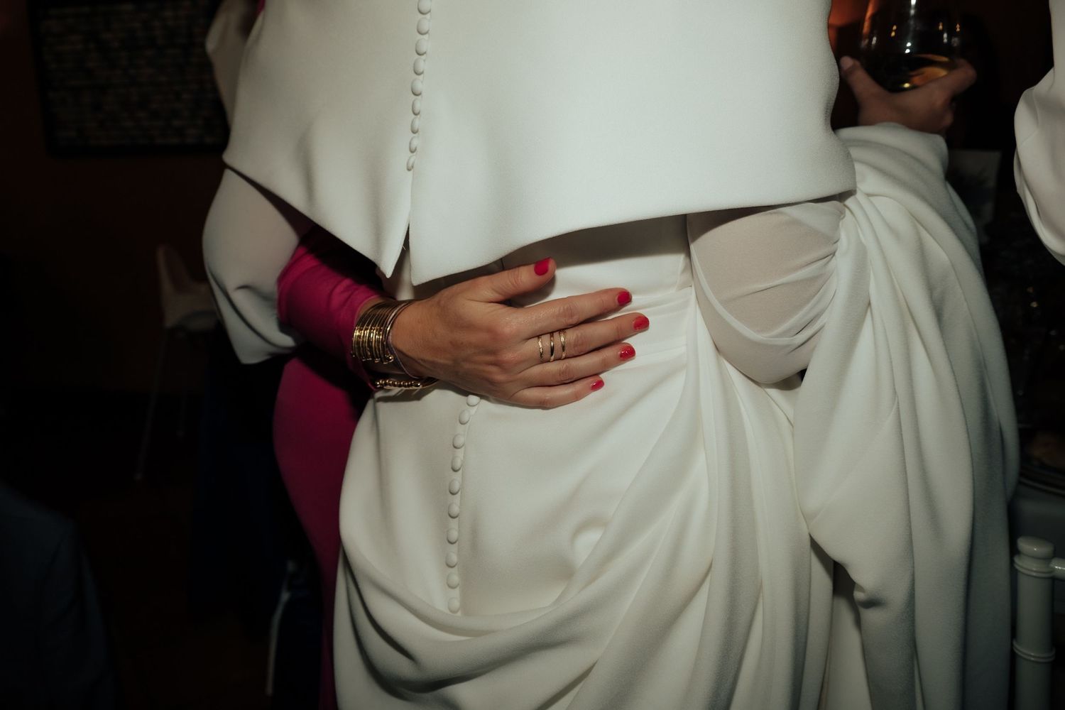Close-up of hands embracing bride in white button-back wedding gown.
