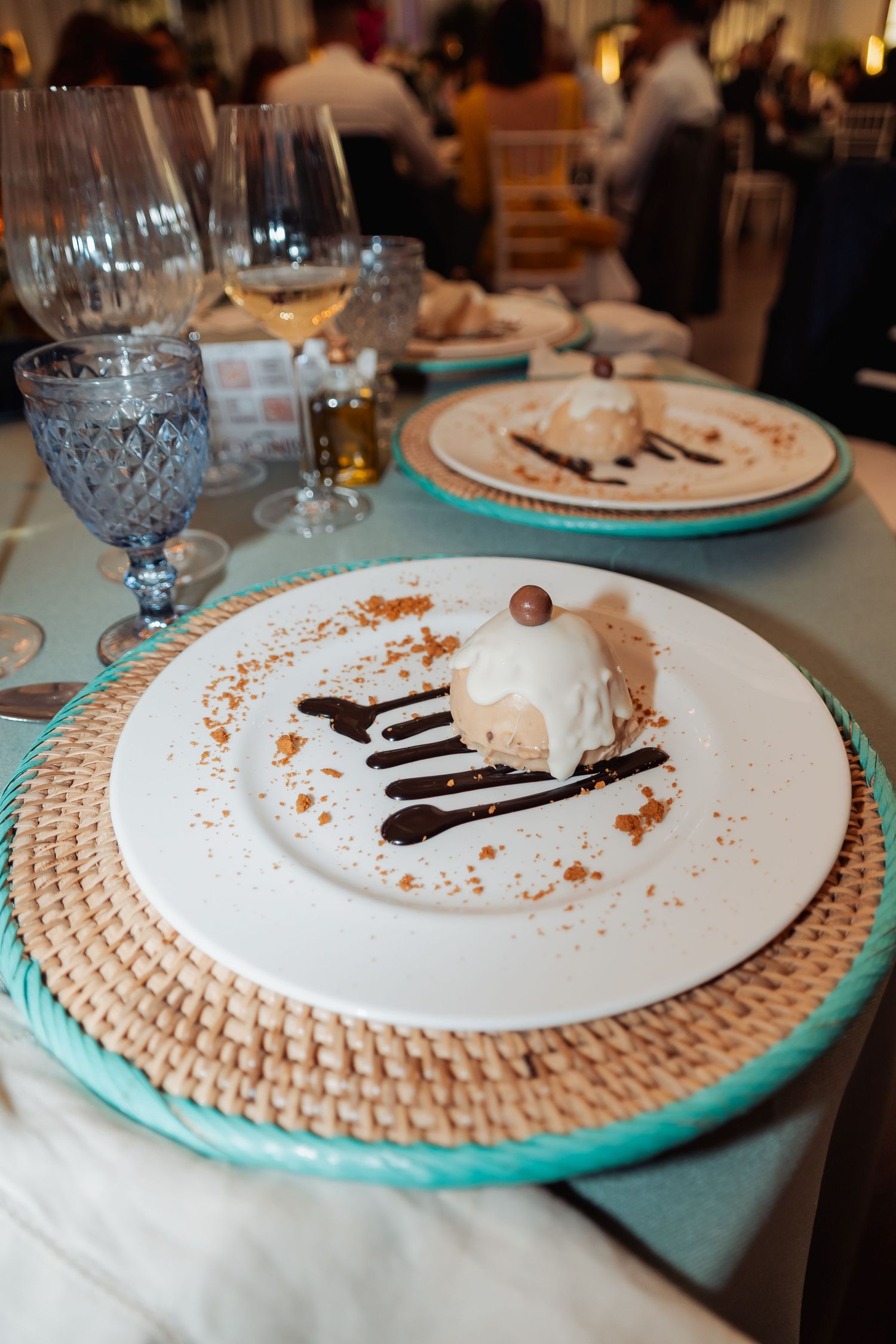 Wedding dessert of vanilla mousse with chocolate drizzle on white plate with wicker charger.