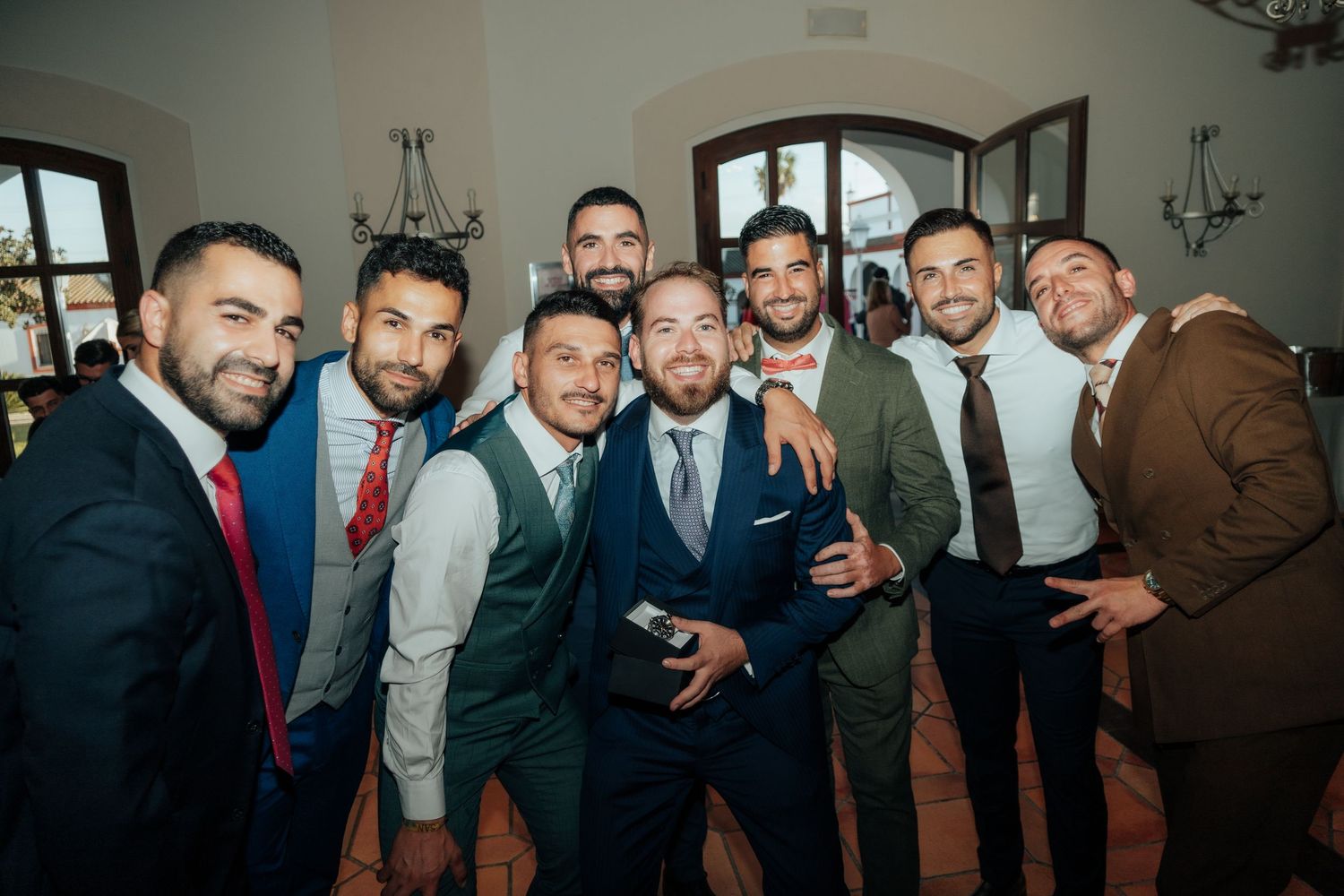 Group of seven well-dressed groomsmen posing together smiling at elegant wedding reception.