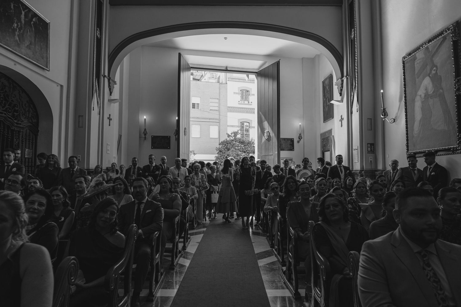 Black and white wide angle view of packed church filled with wedding guests during ceremony.