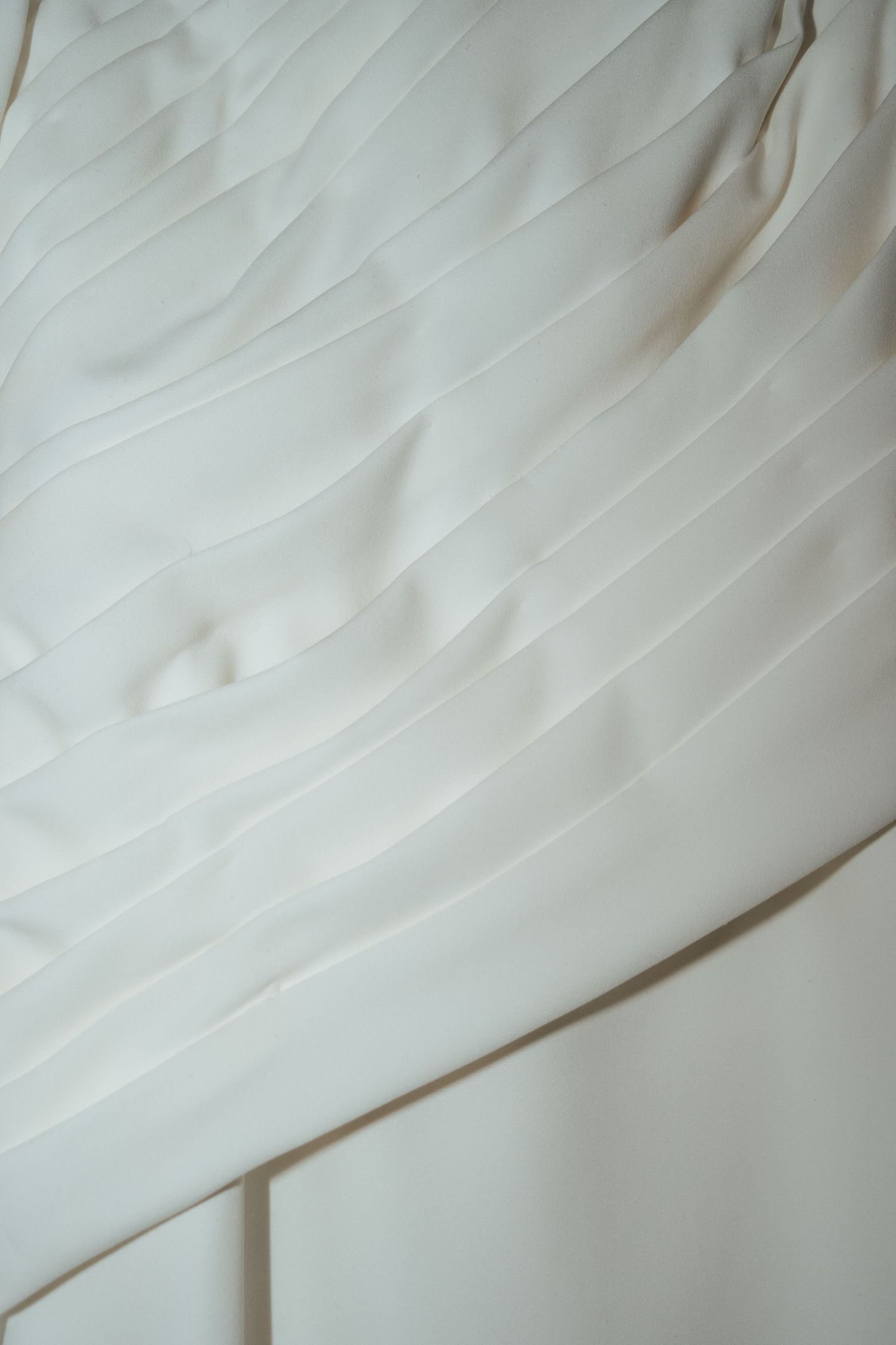 Close-up detail of delicate pleated fabric on an elegant ivory white wedding dress bodice.