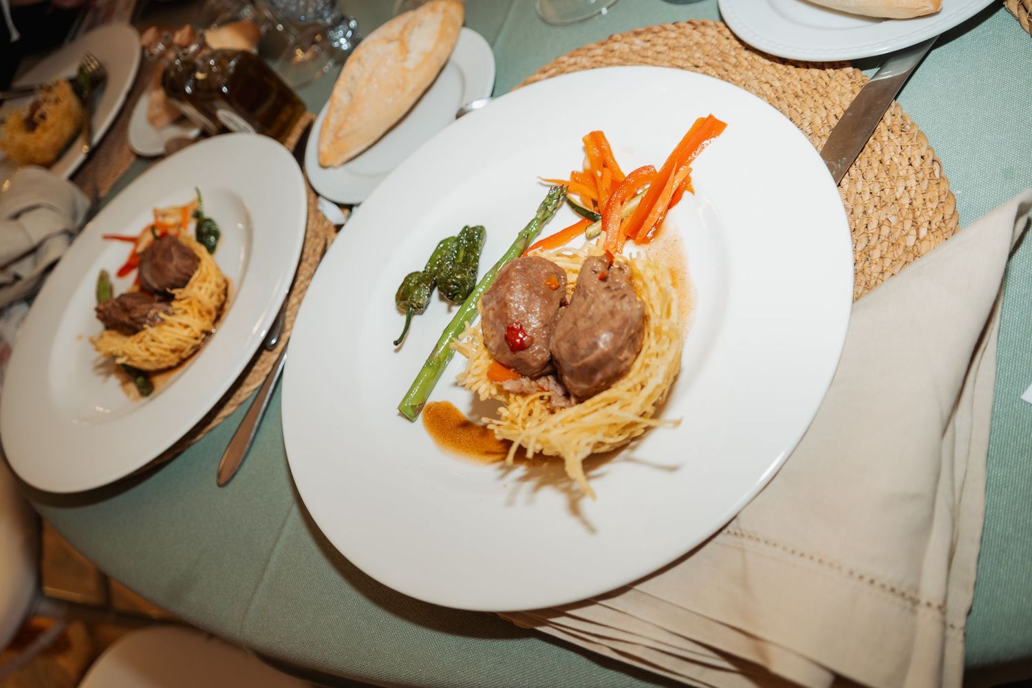 Elegantly plated wedding reception dish with meat, pasta, asparagus and colorful vegetable garnish.