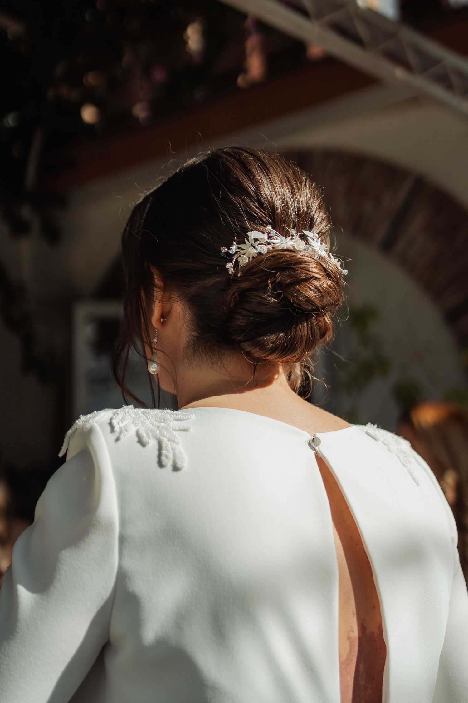 Close-up of bride's chic low bun with crystal hairpiece and open-back white gown.