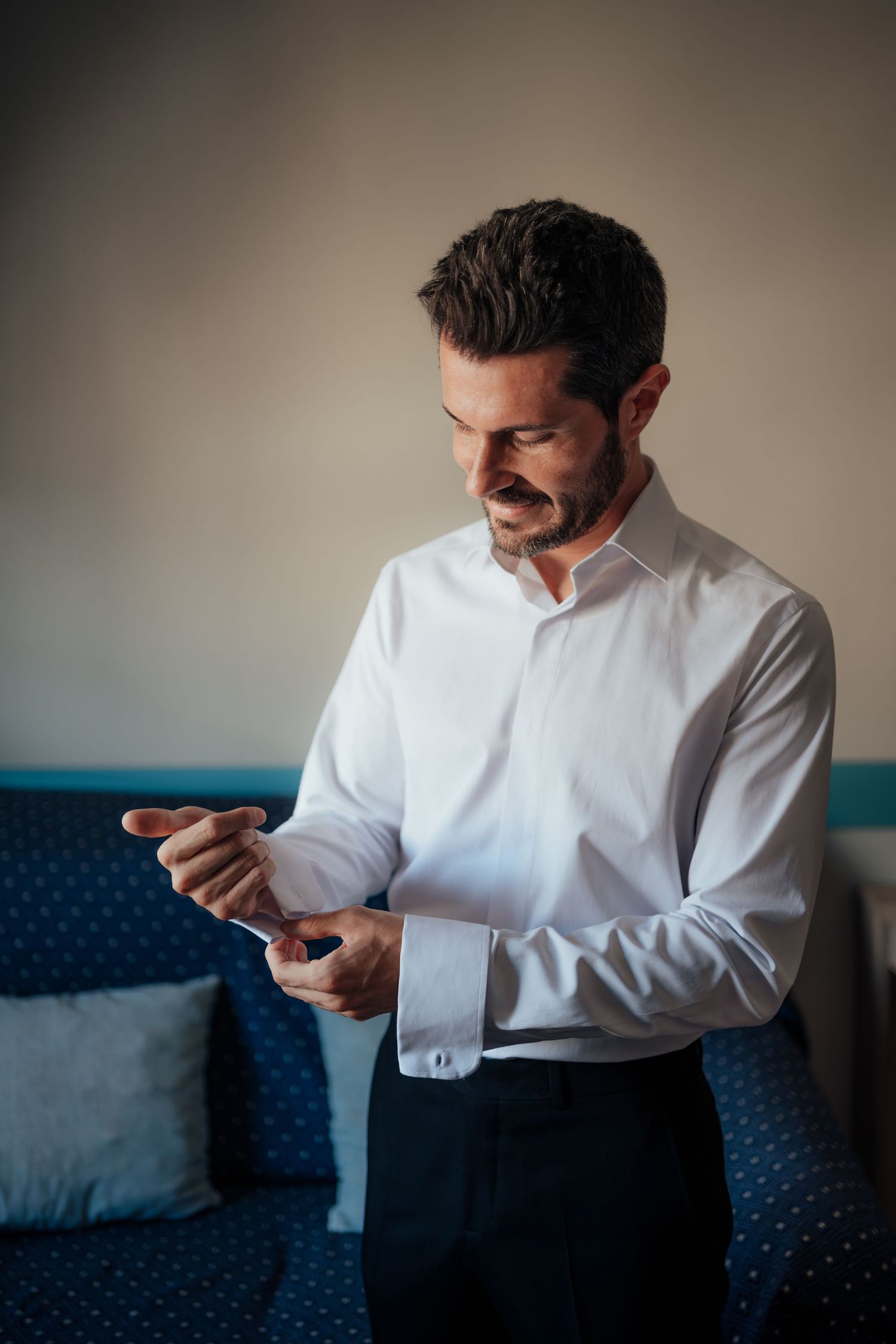 Groom in white dress shirt fastening cufflinks while getting ready for wedding.