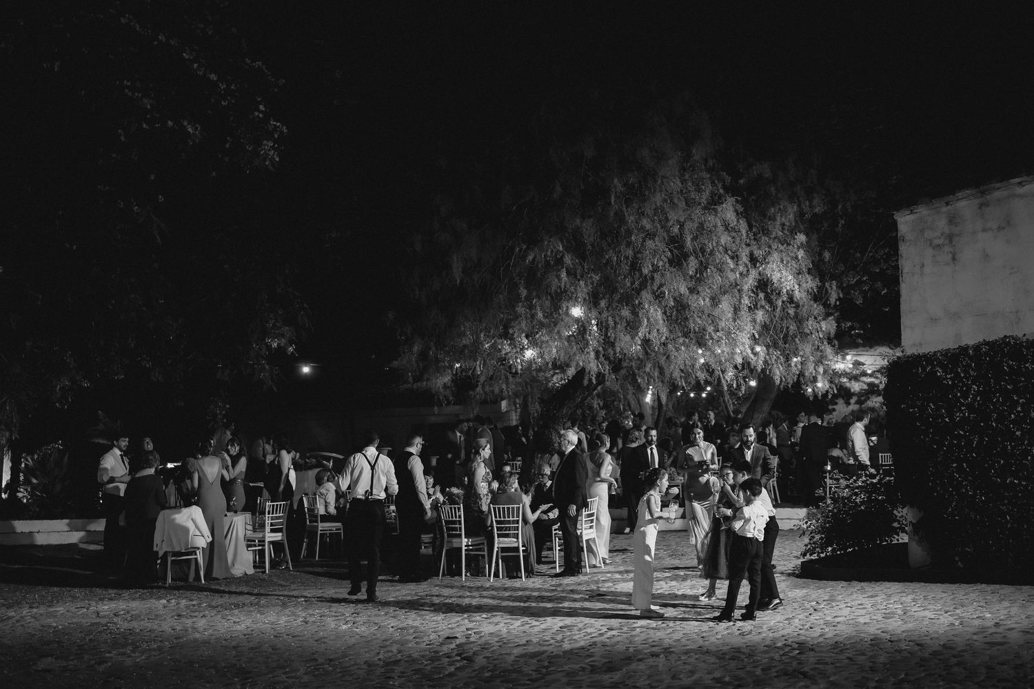 Black and white wide shot of guests mingling at an elegant outdoor nighttime event.