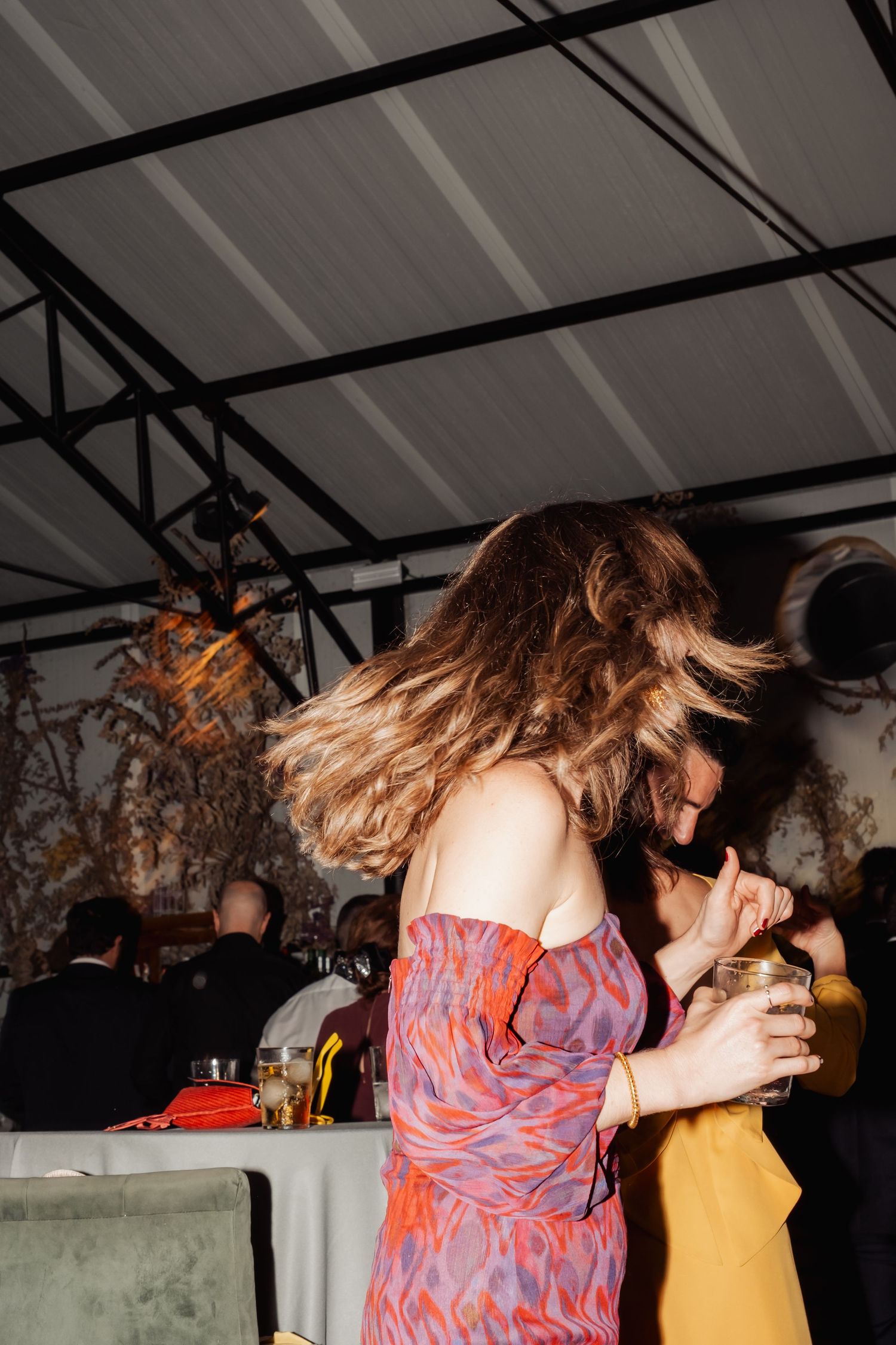 Woman in colorful off-shoulder dress dancing energetically with flowing hair at a festive evening reception.