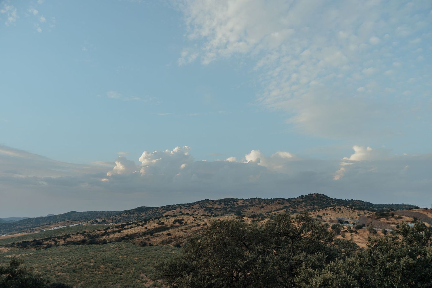 Panoramic view of rolling hills and sparse vegetation under a partly cloudy blue sky.