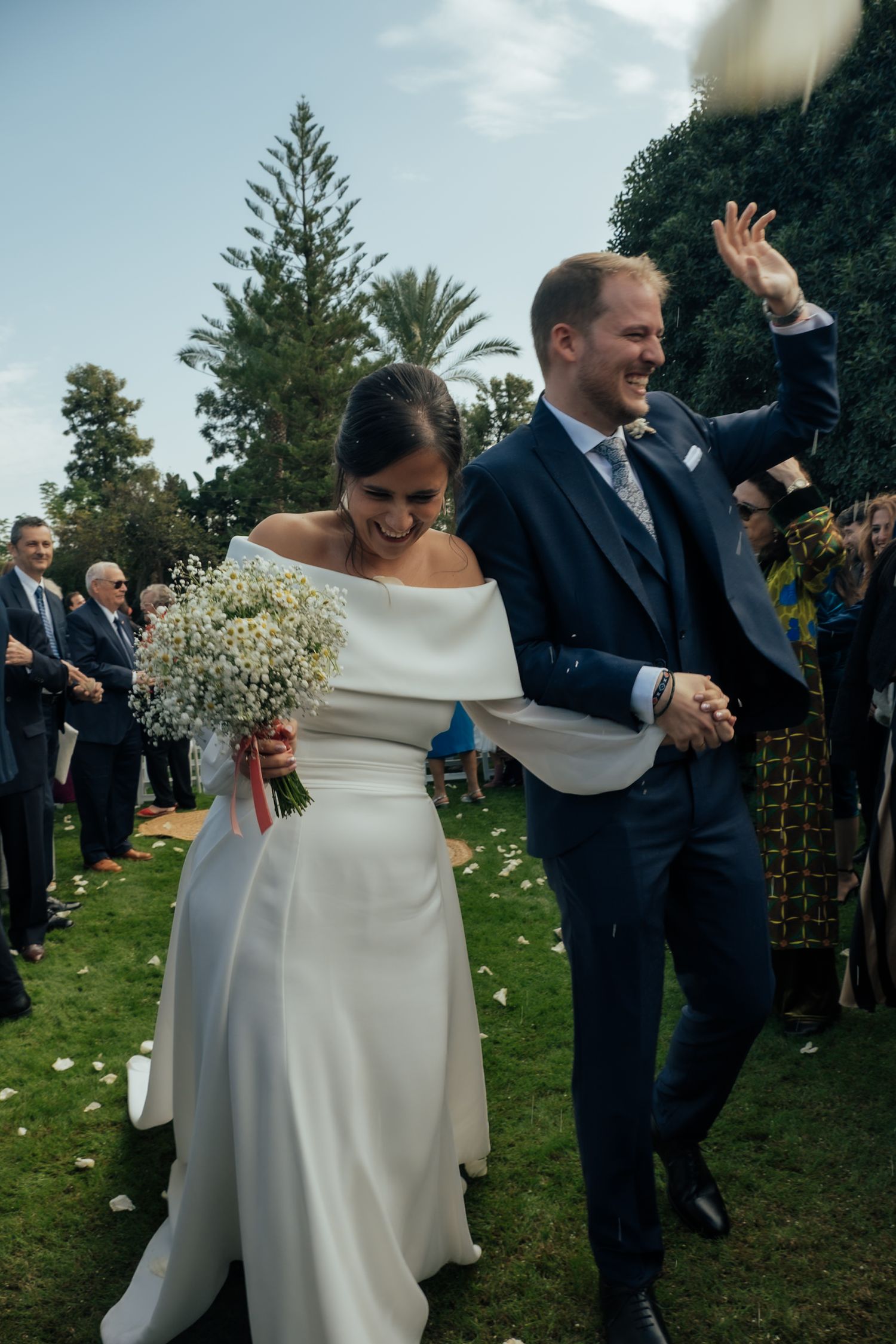 Joyful bride and groom walking down the aisle after ceremony as guests toss white flower petals.