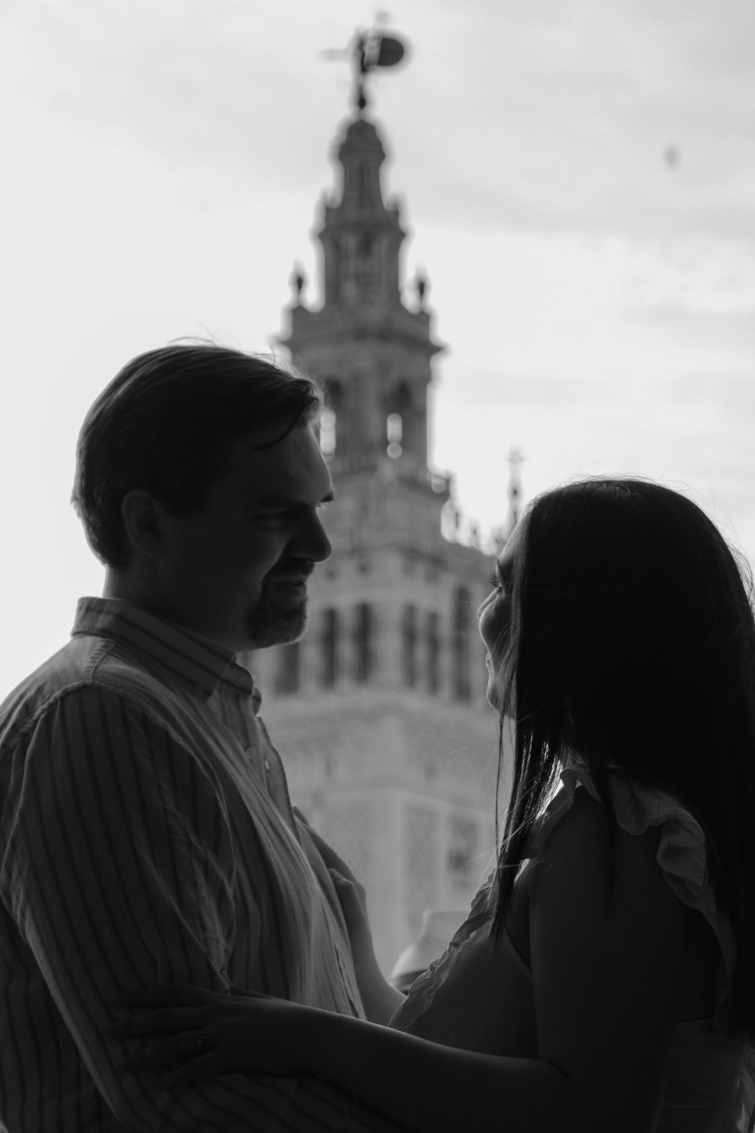 Black and white silhouette of couple facing each other with historic cathedral tower behind.