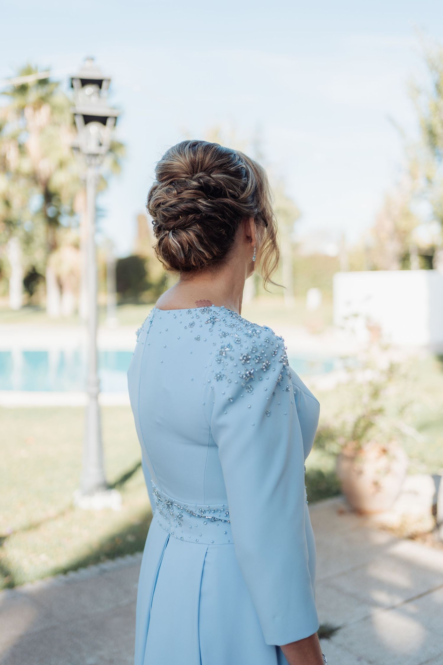 Back view of bride in light blue beaded gown with intricate updo hairstyle near pool.