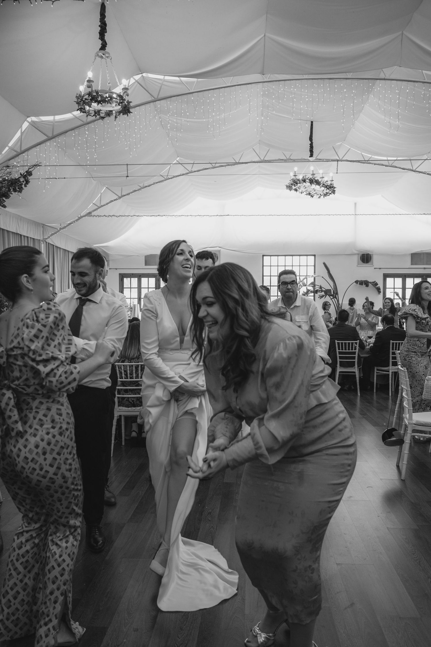 Black and white photo of wedding guests dancing joyfully in a decorated marquee reception venue.