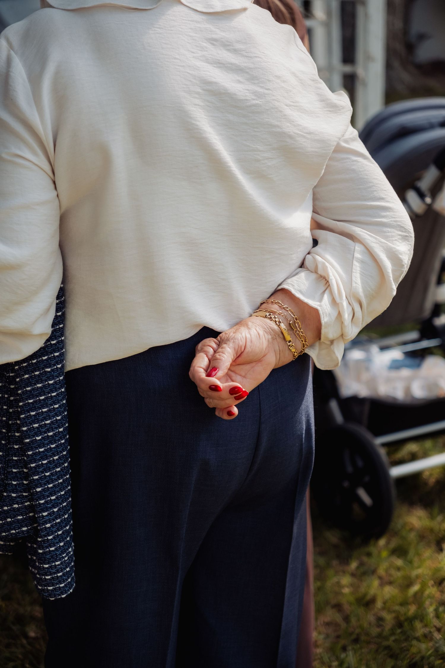 Close-up of an elderly woman's hands clasped behind her back adorned with gold bracelets.