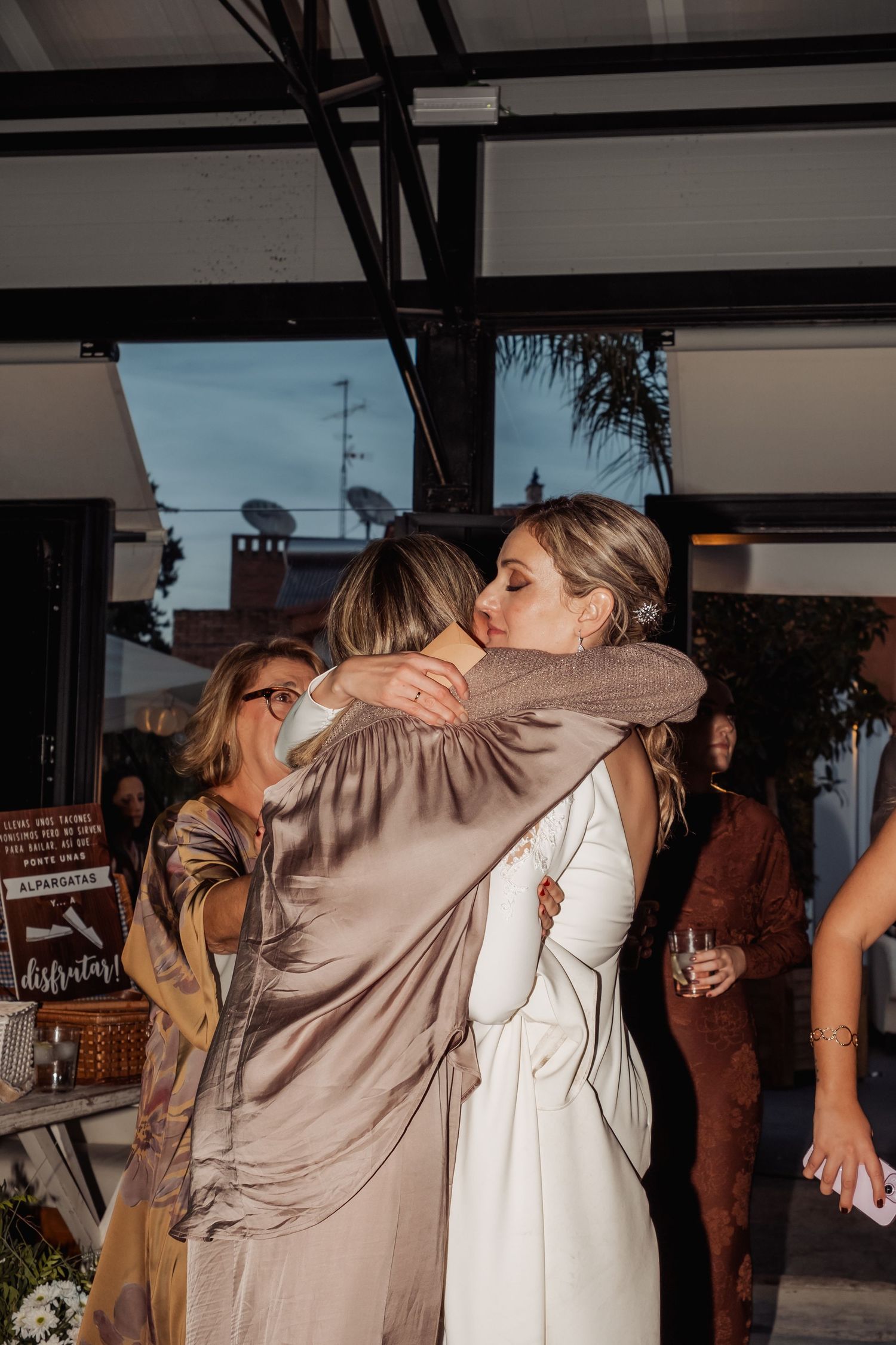 Bride in white wedding dress sharing a warm embrace with a guest at her wedding reception.