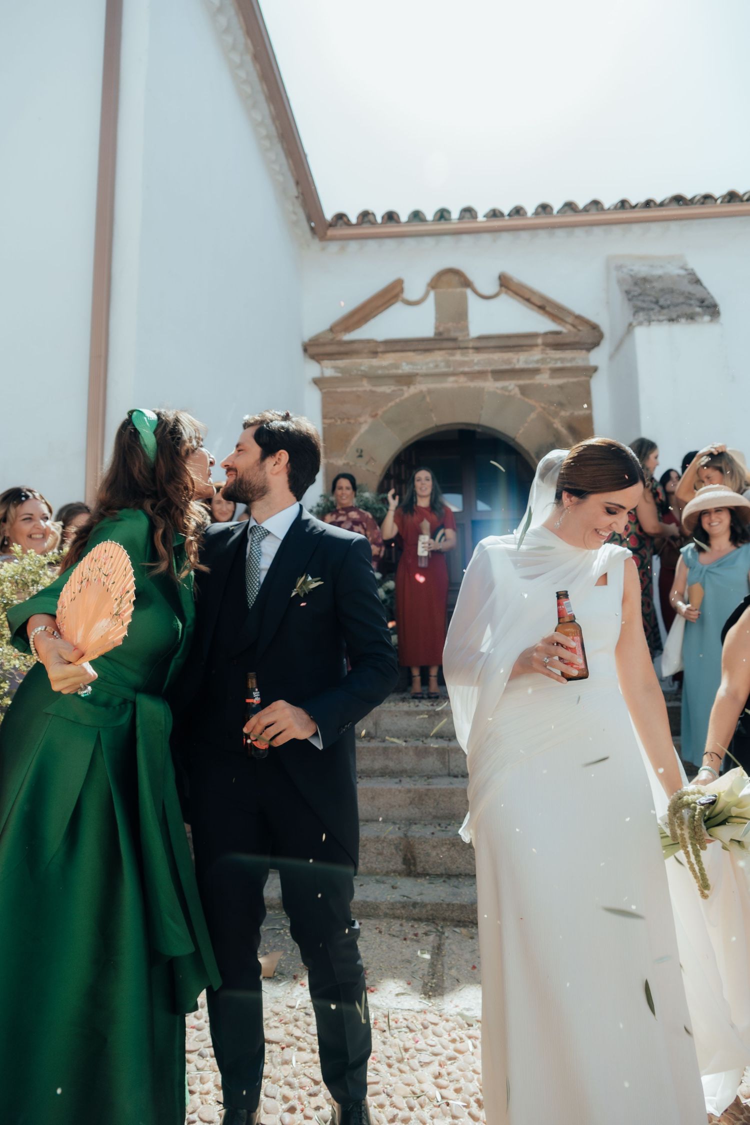 Newlywed couple walking out of a white Spanish church surrounded by smiling guests after the ceremony.