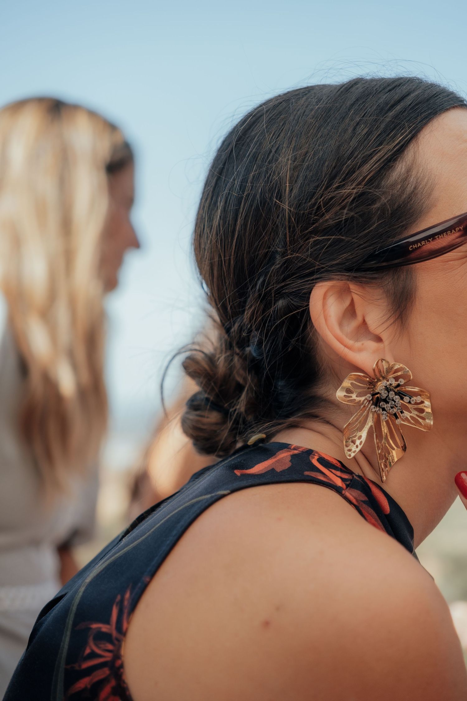 Close-up of woman wearing large gold floral earring with braided updo at outdoor event.