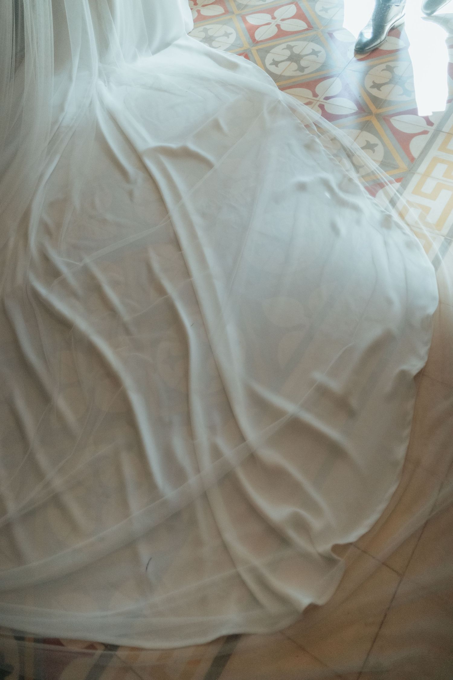 Close-up artistic shot of bride's flowing white wedding veil and gown draped over tiled floor.