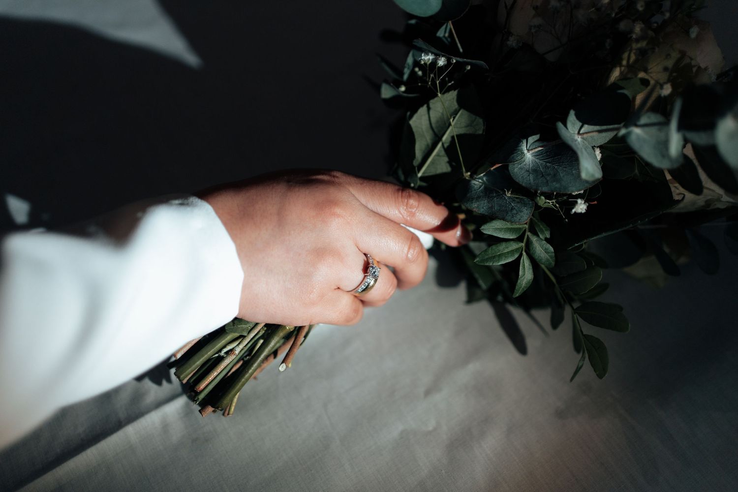 Bride holding dark green eucalyptus bouquet with silver ring on her finger.