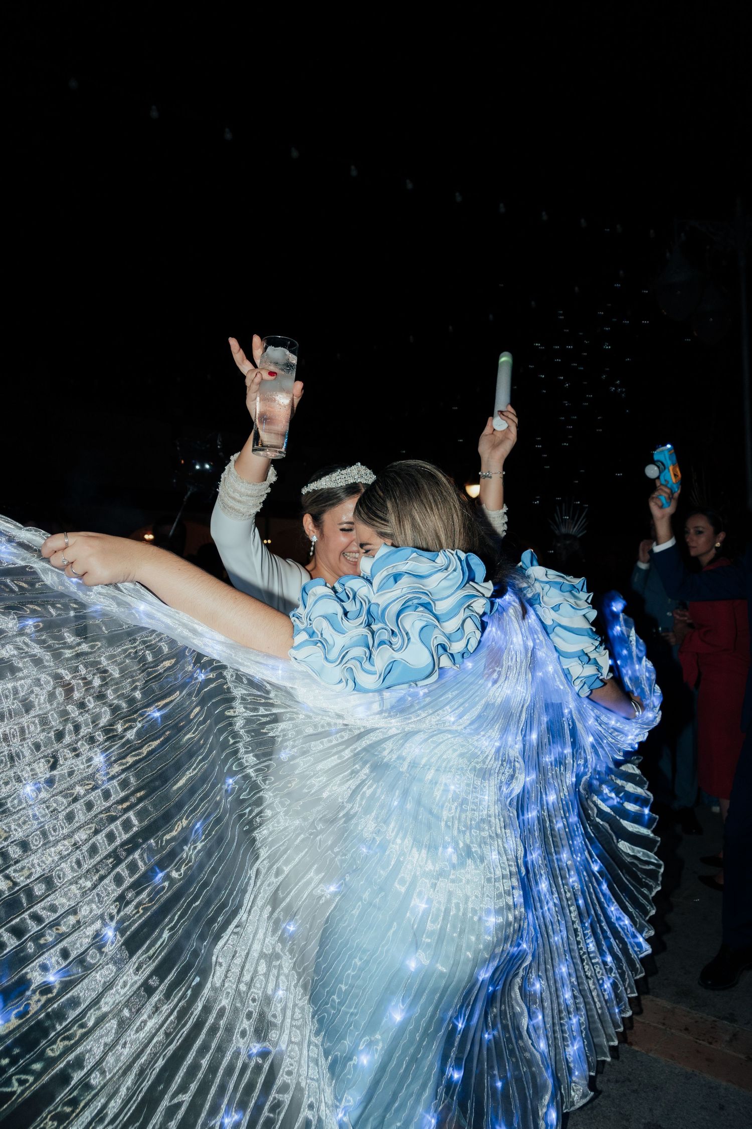 Two women dancing in glowing LED butterfly wings at an outdoor night event.