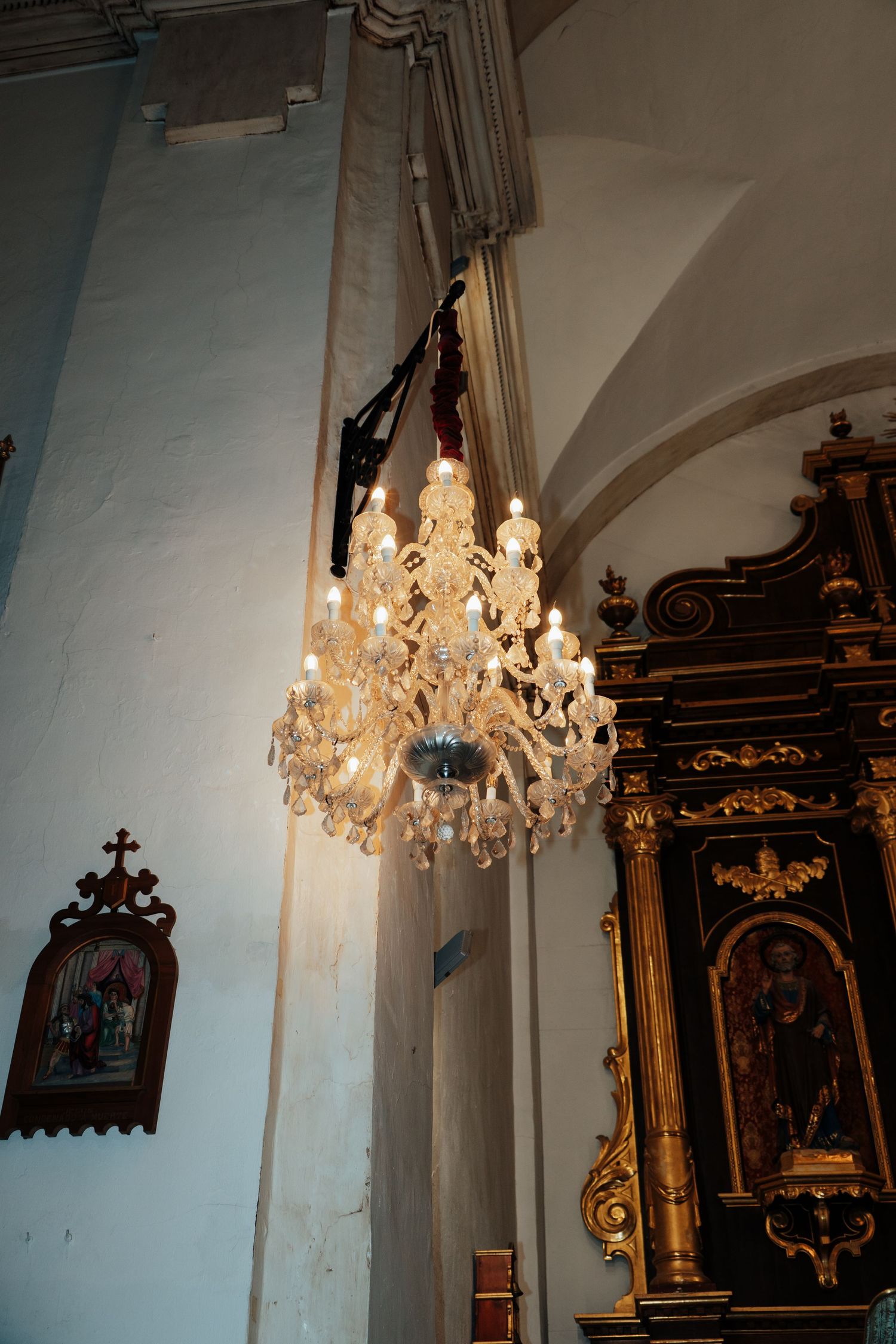 Ornate crystal chandelier hanging in historic church interior with gilded altar and arched ceiling.