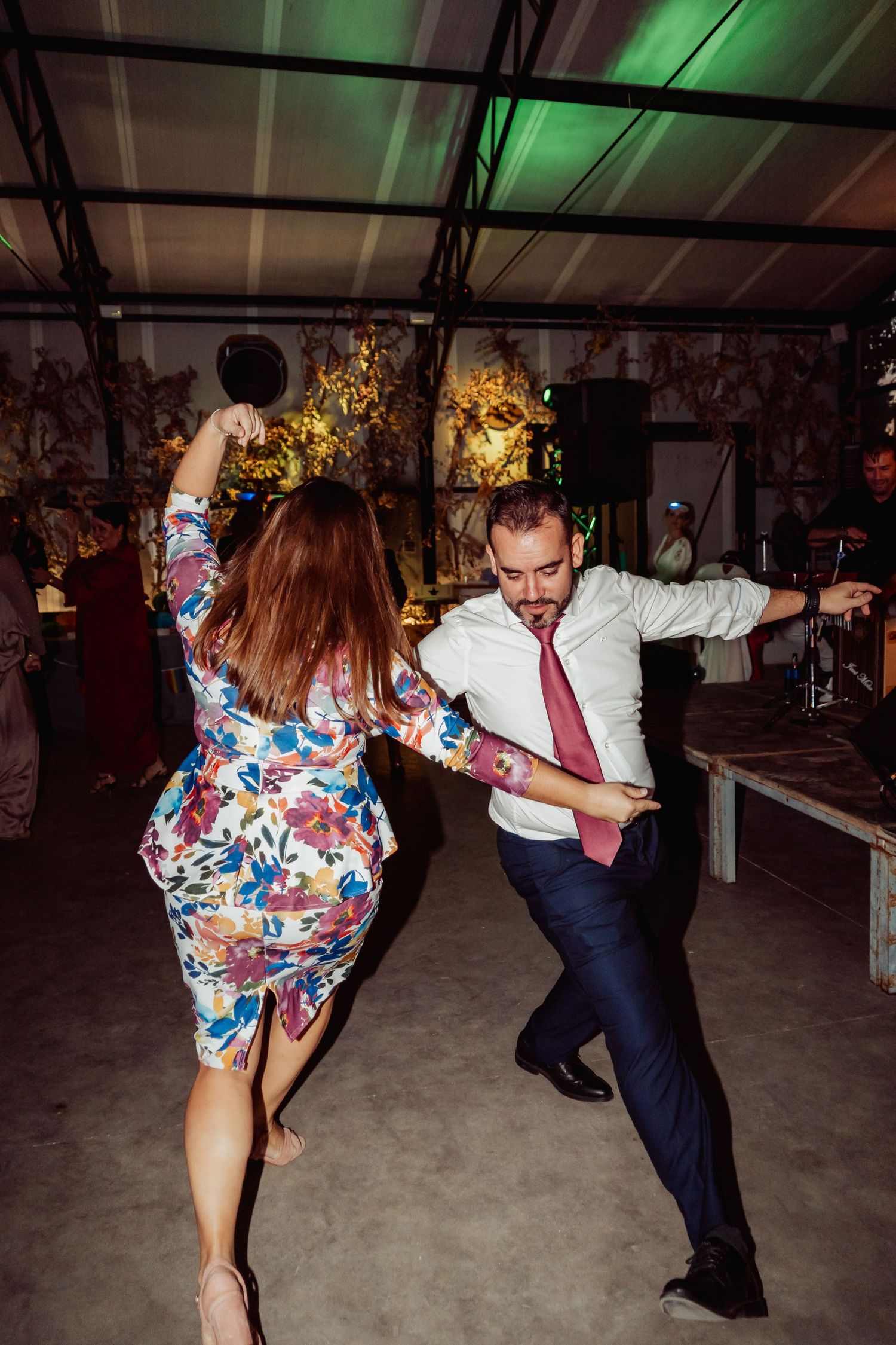 Energetic couple dancing at a wedding party, man in white shirt and tie, woman in floral dress.