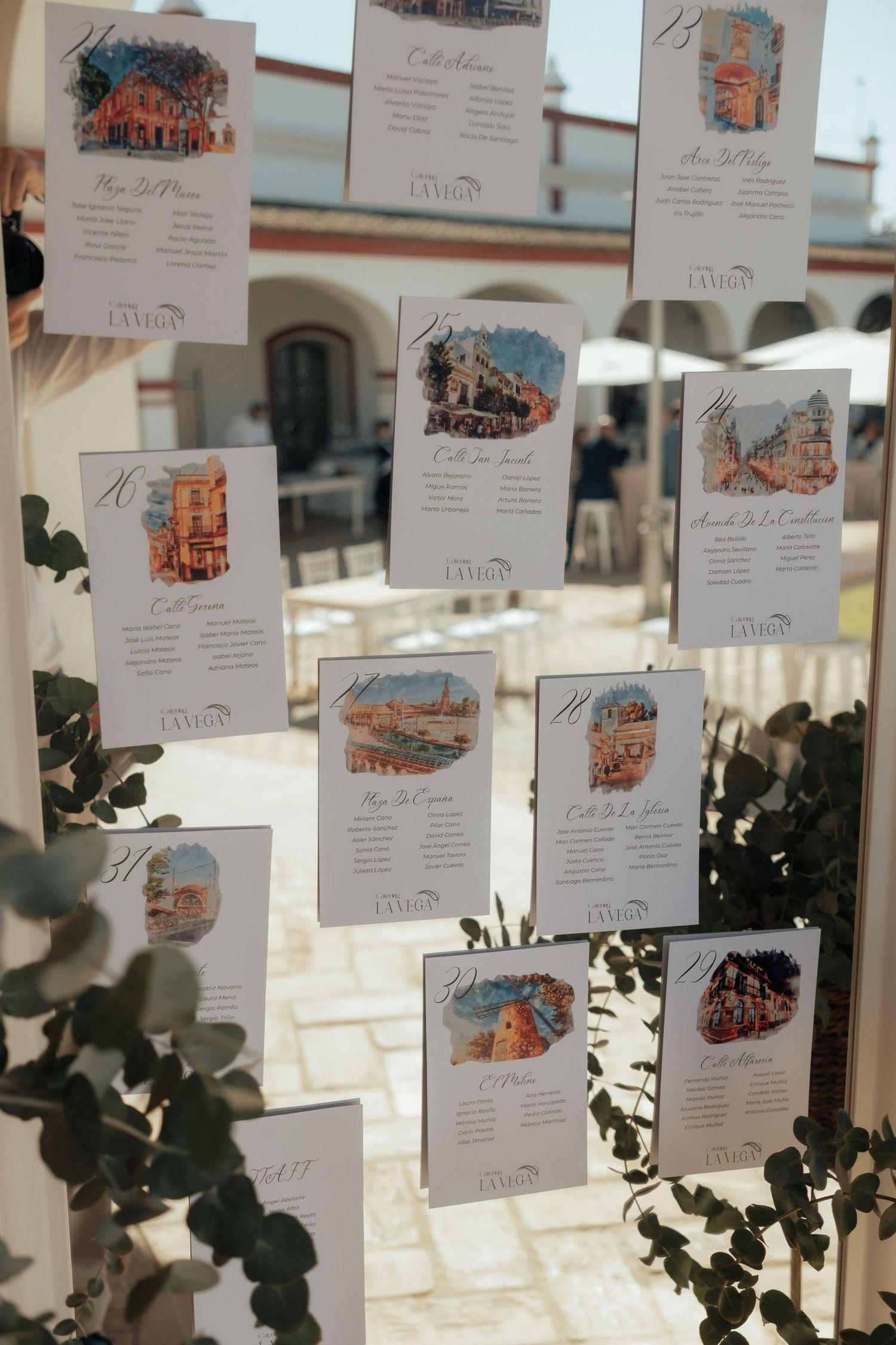 Elegant wedding seating chart cards with watercolor illustrations displayed on a decorative stand outdoors.