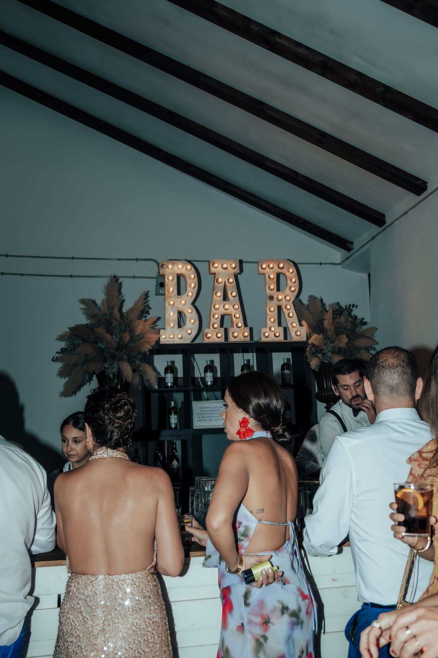 Guests gathered at illuminated BAR sign with marquee lights at elegant wedding reception.