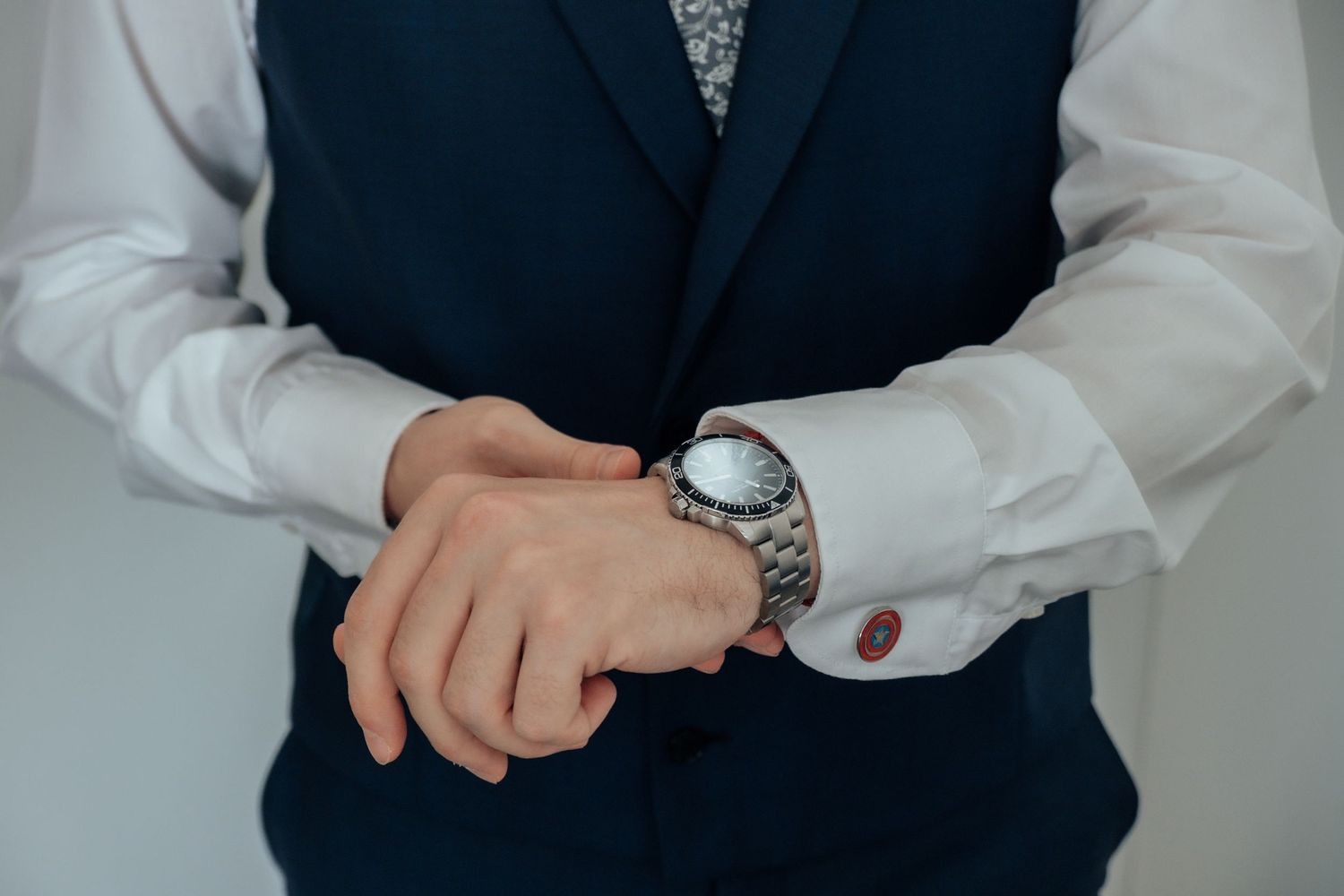 Groom in a navy vest and white shirt adjusting his silver watch and cufflinks before the wedding ceremony.