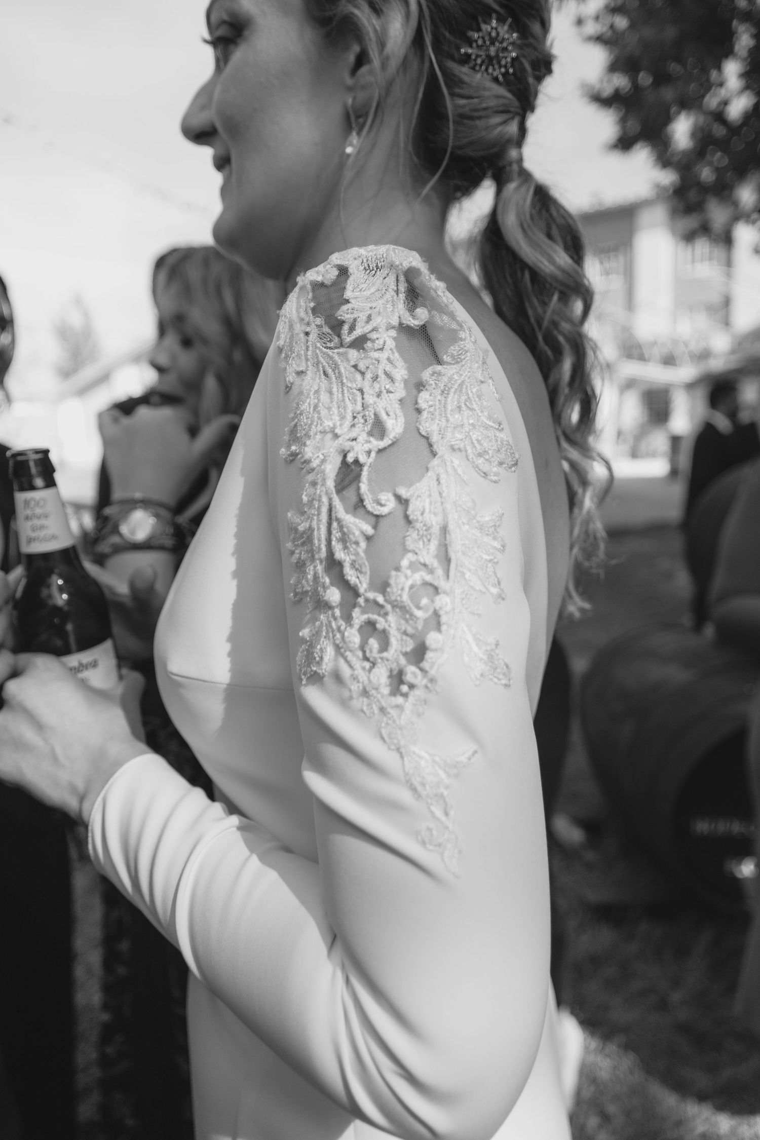 Black and white close-up of bride's lace sleeve detail on elegant wedding gown.