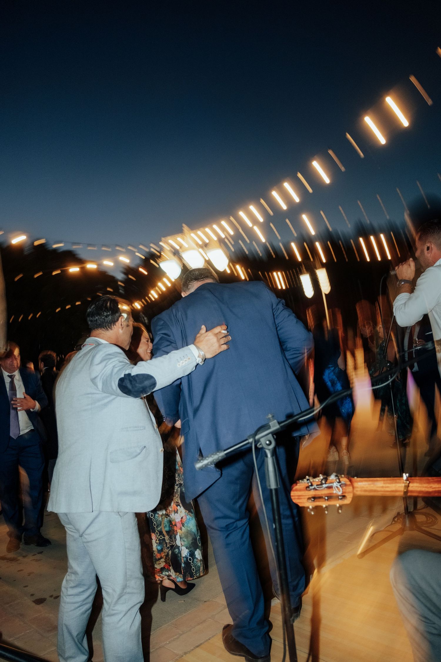 Guests dancing and celebrating at outdoor evening wedding reception with string lights.