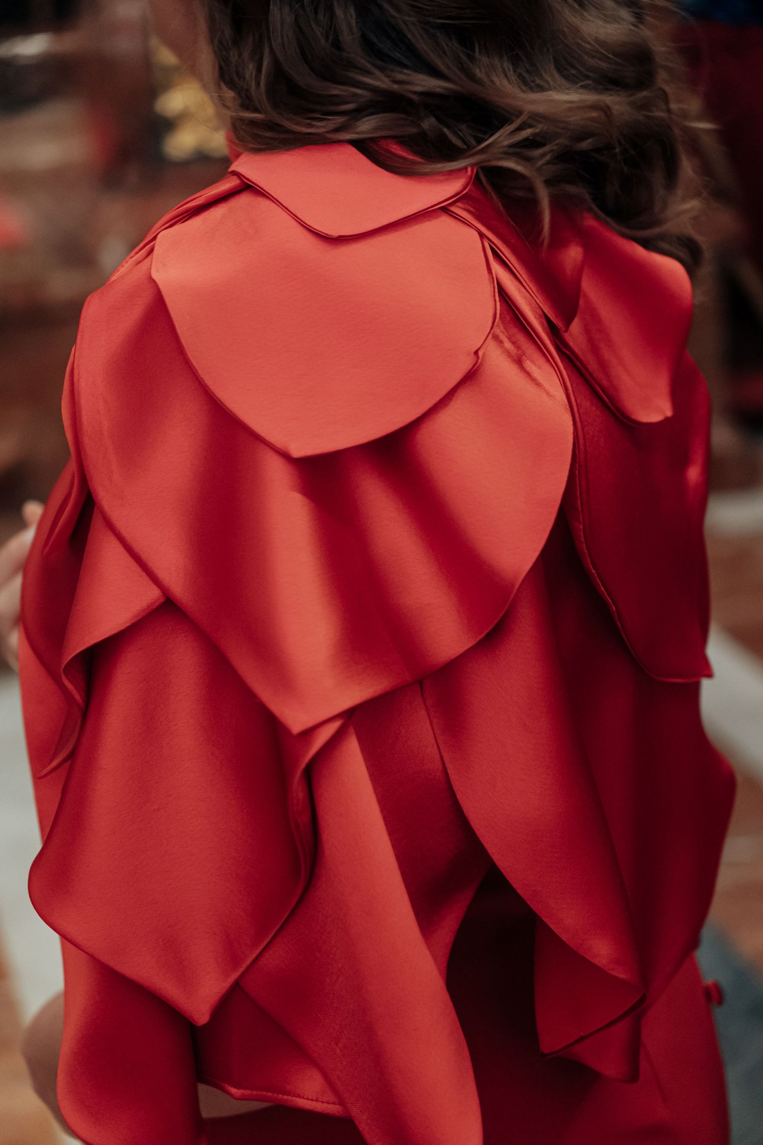Back view of woman in red dress with layered scalloped ruffle detail on shoulders and sleeves.