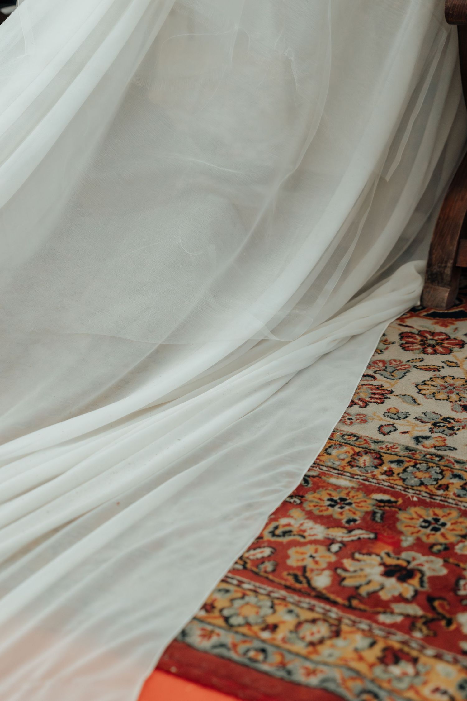 White wedding dress train draped elegantly over a colorful traditional Persian rug on the floor.