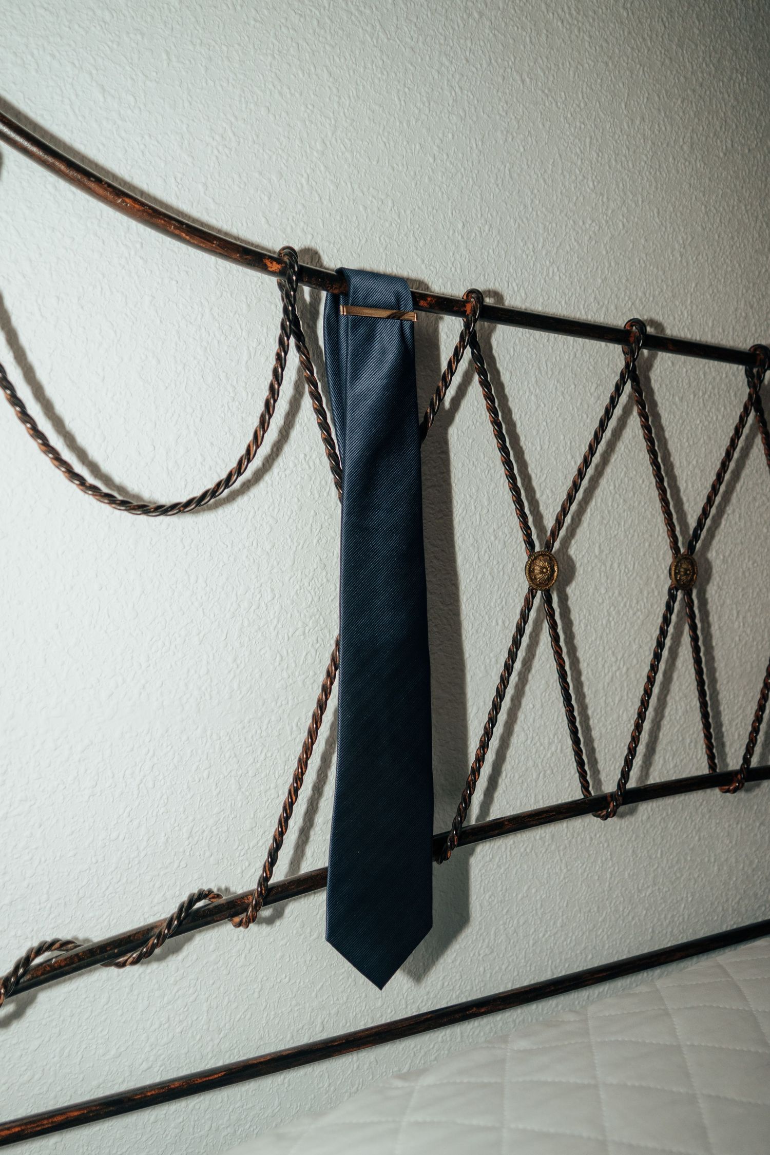 A dark navy blue necktie hangs on a decorative wrought iron headboard with rope details.