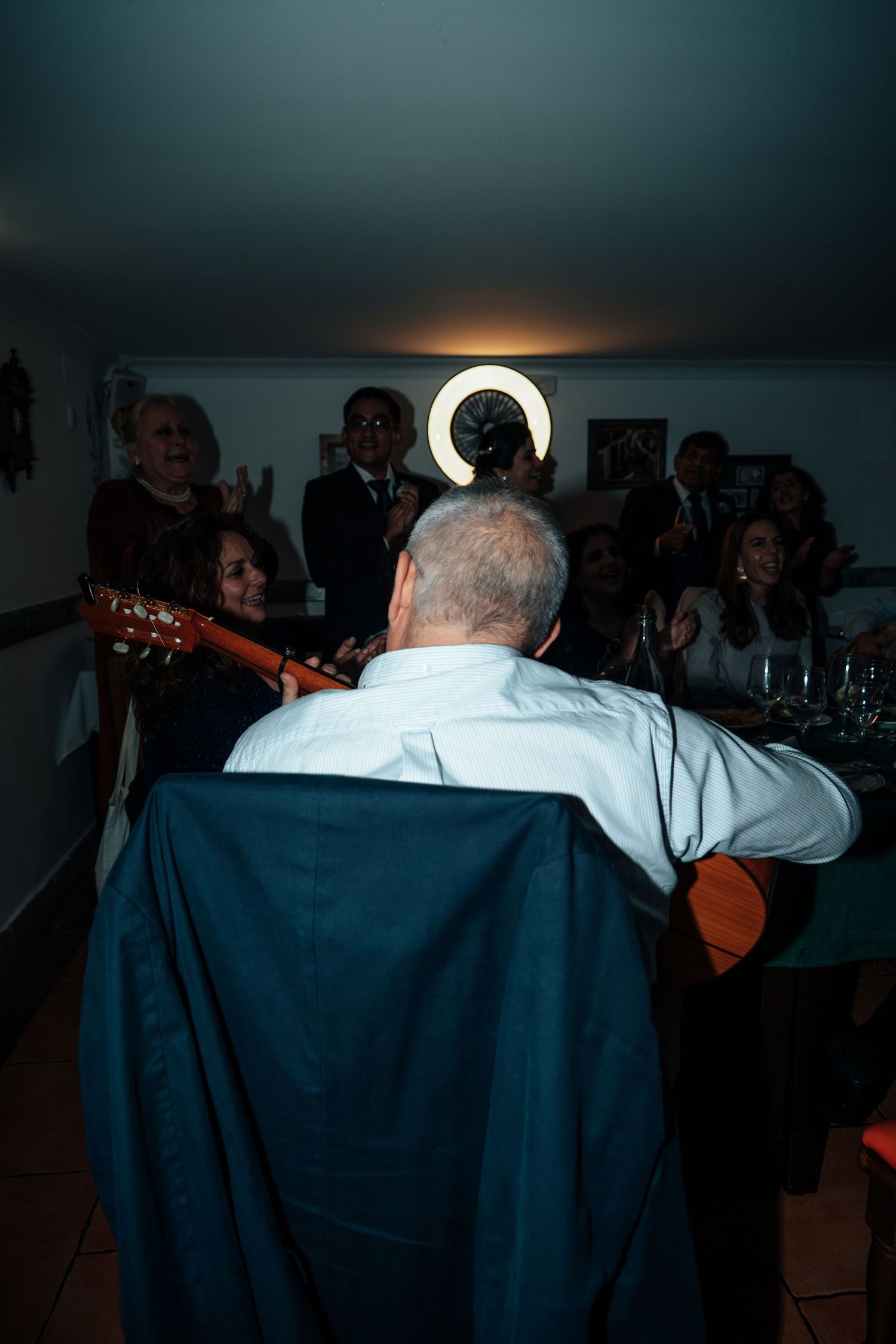 Guest playing acoustic guitar for a group of celebrating guests at an indoor wedding reception.