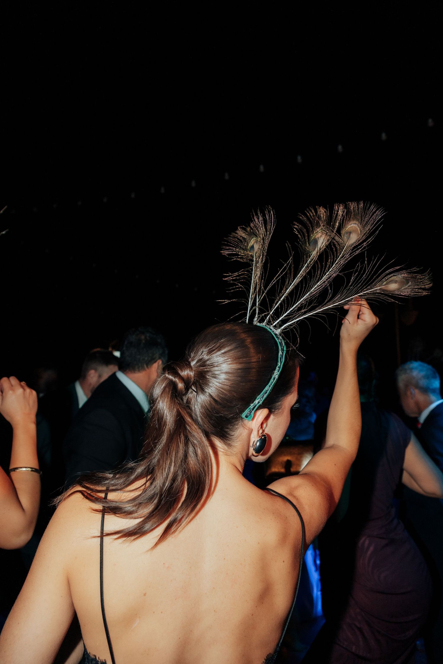 Woman with peacock feather hair accessory dancing at a formal evening event.