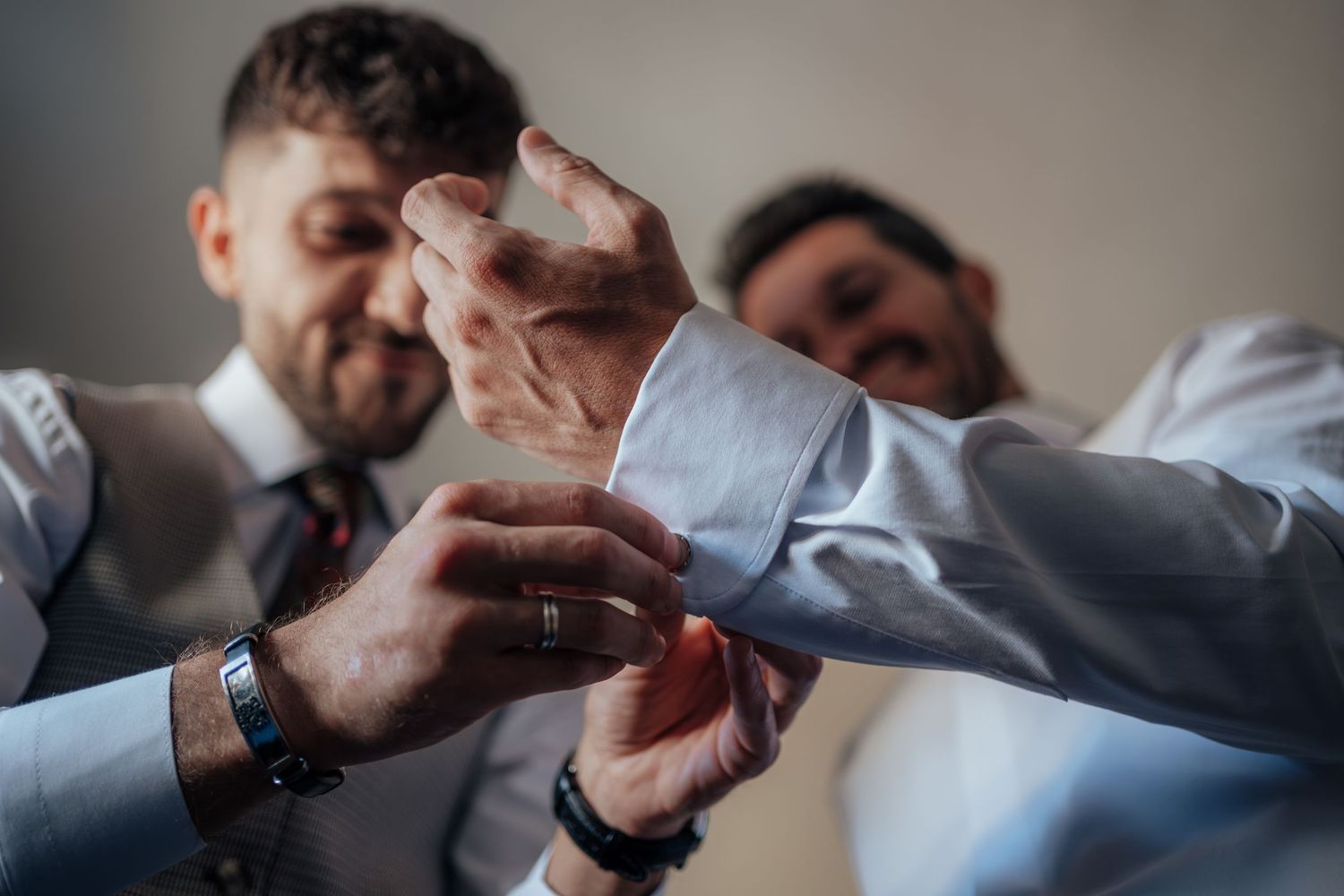 Groomsmen smiling and helping groom fasten cufflinks while getting ready for wedding.