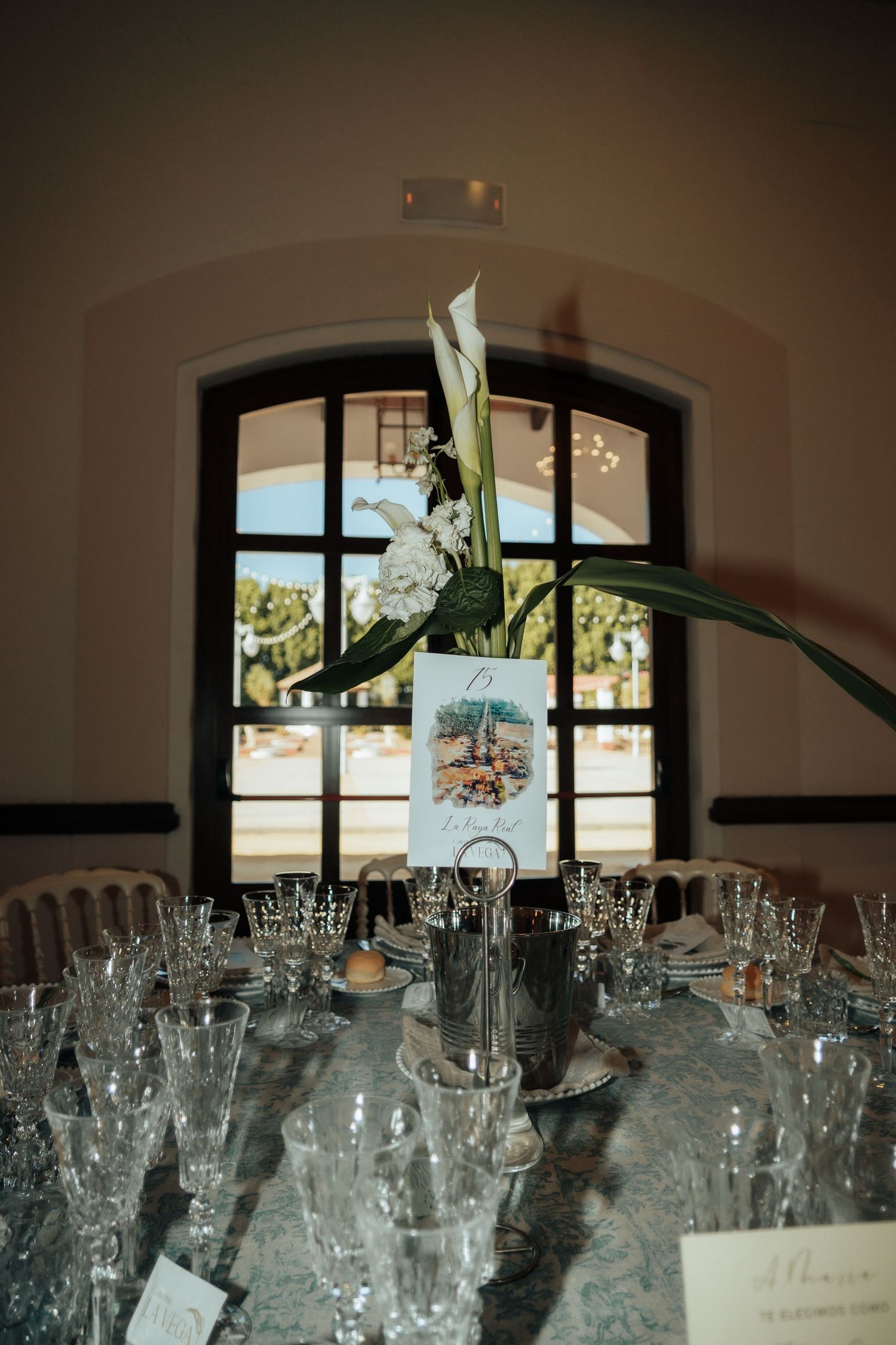 Elegant wedding table centerpiece with white calla lilies and crystal glassware in a grand venue.