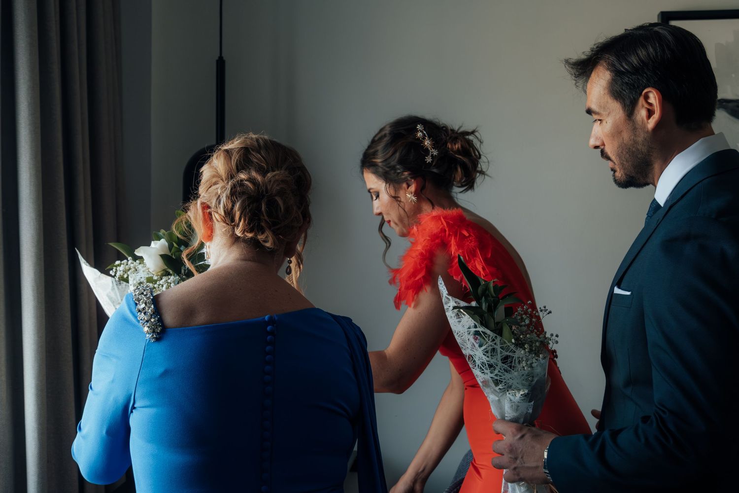 Guests exchanging floral bouquets during wedding preparations in a bright modern hotel room.