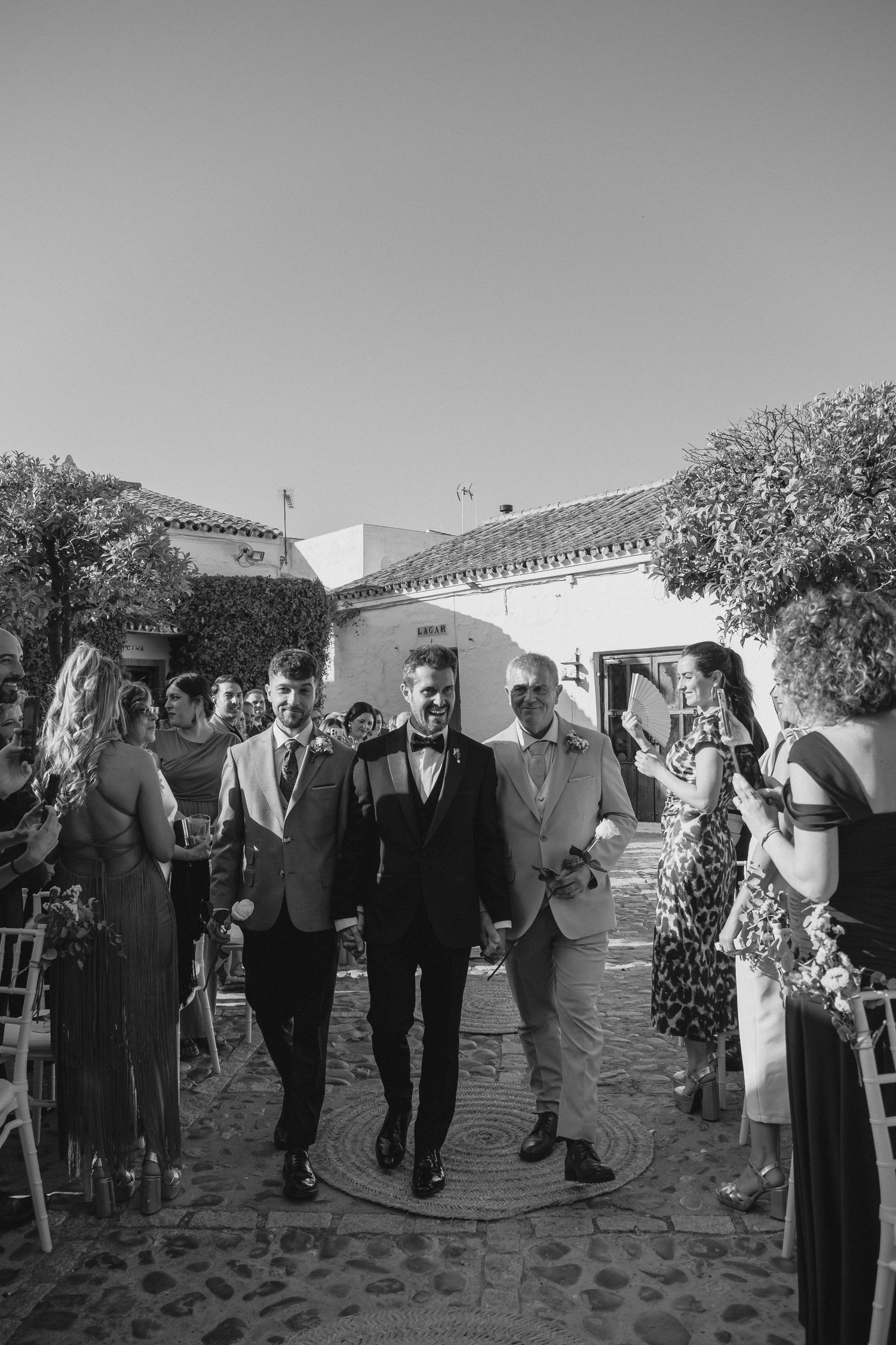 Two grooms walk hand in hand down the aisle after their outdoor wedding ceremony in black and white.