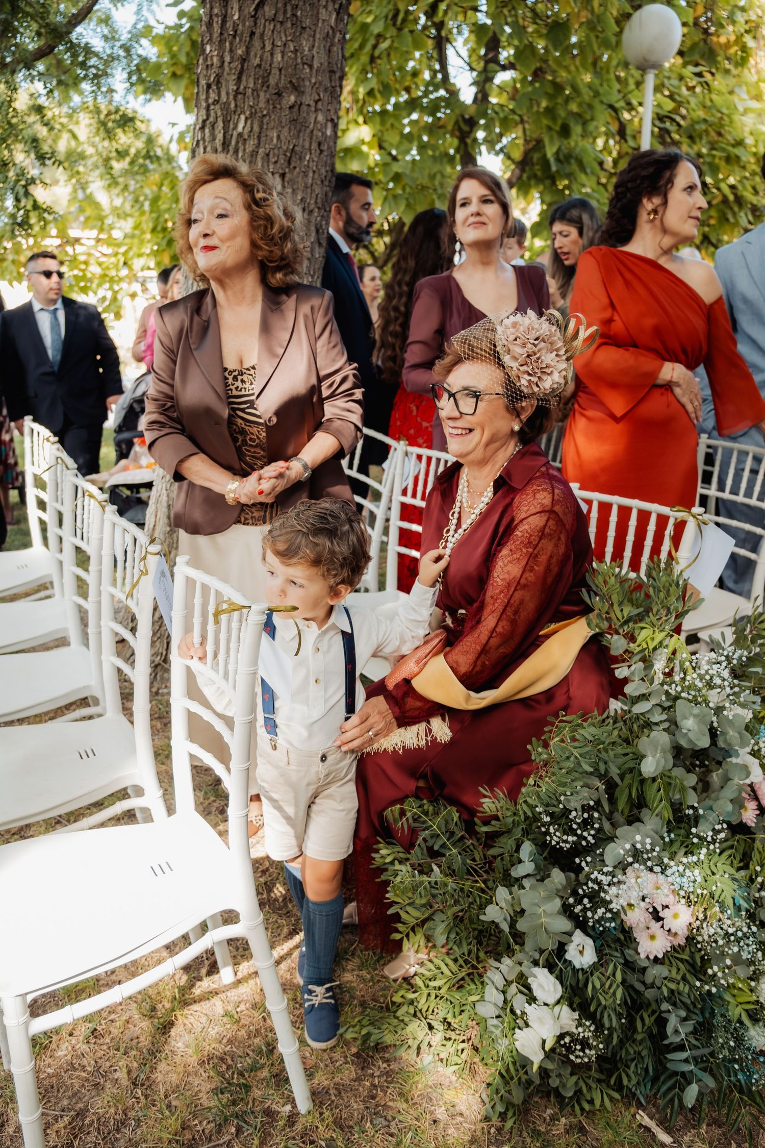 Wedding guests including elderly woman and young boy seated at outdoor garden ceremony.