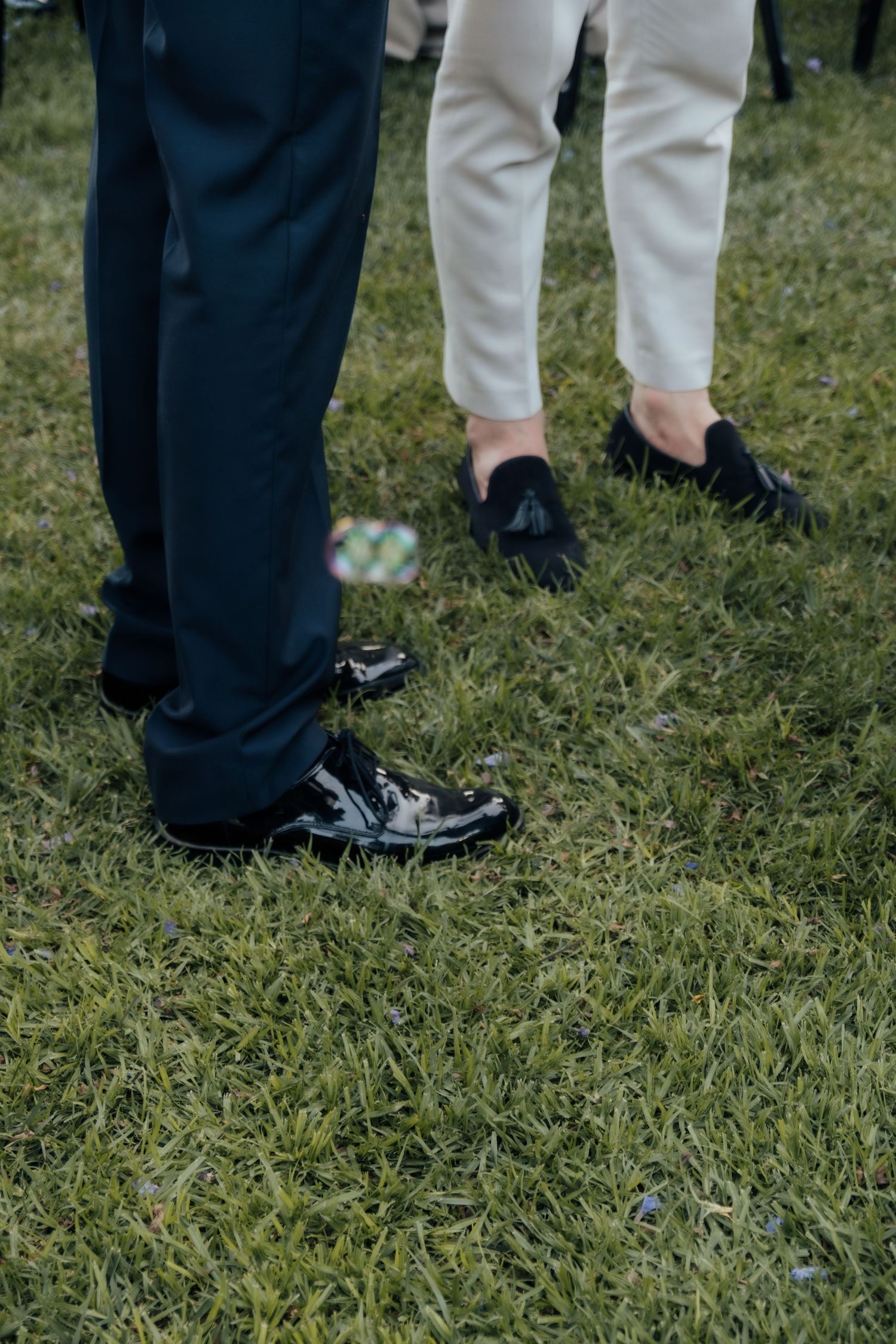 Close-up of two men's dress shoes on grass, one in black patent leather oxfords, one in black loafers.