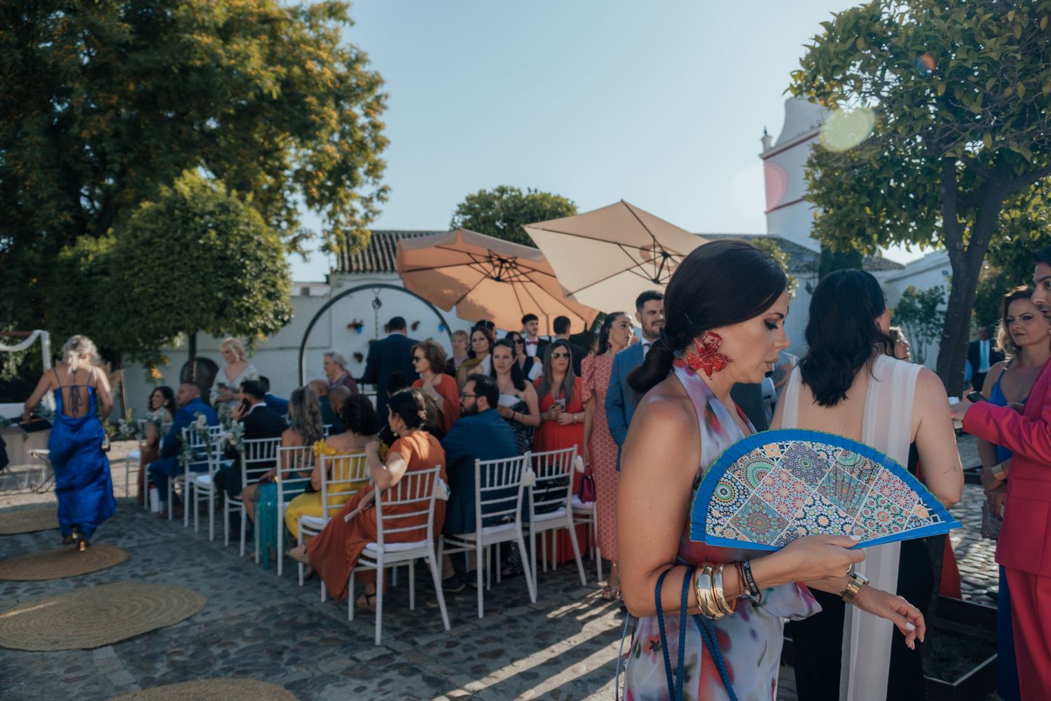 Colorfully dressed wedding guests mingling at a vibrant outdoor ceremony with hand fans.