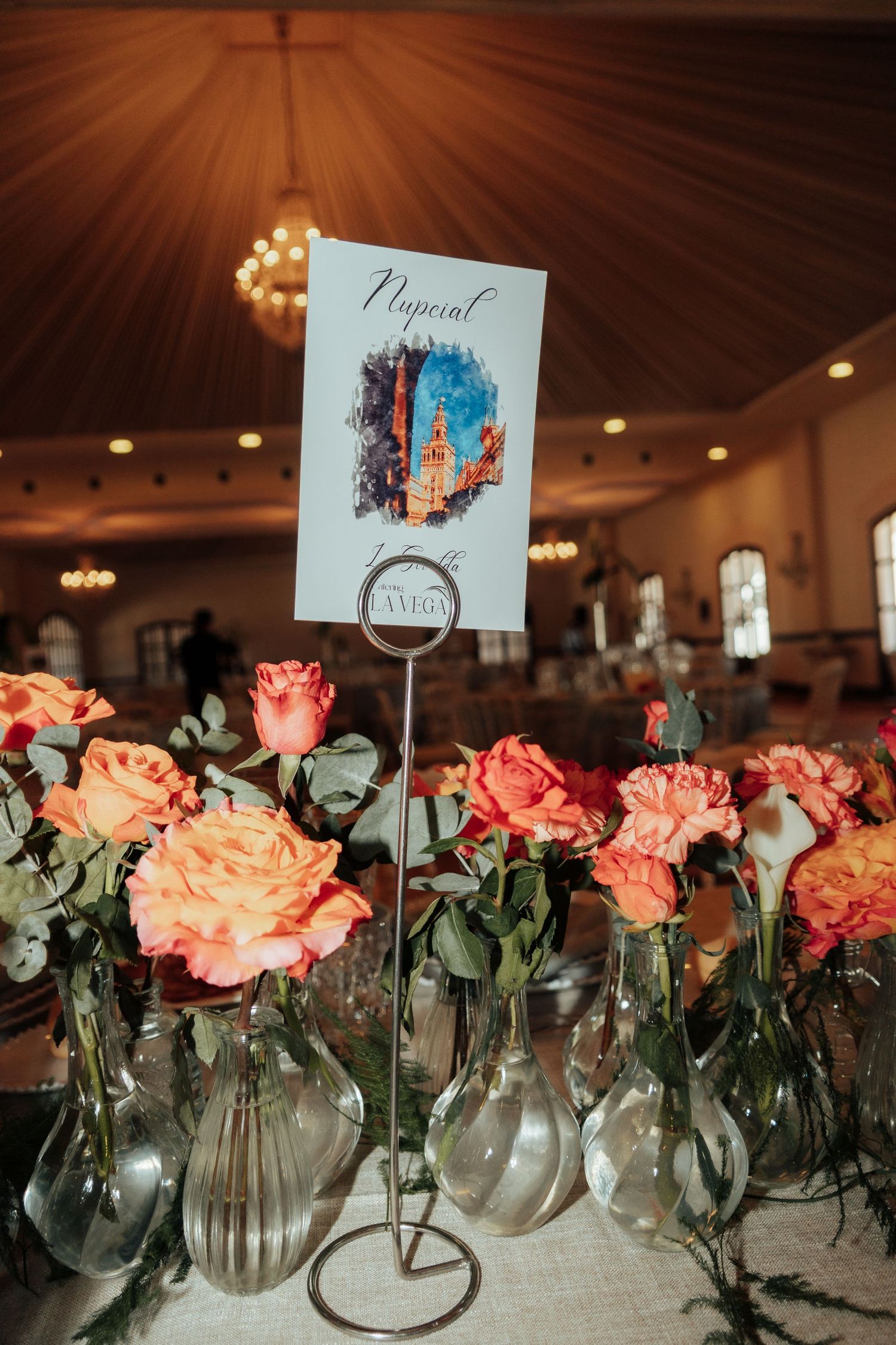 Wedding table centerpiece featuring peach roses in glass vases with a Seville-themed table card.