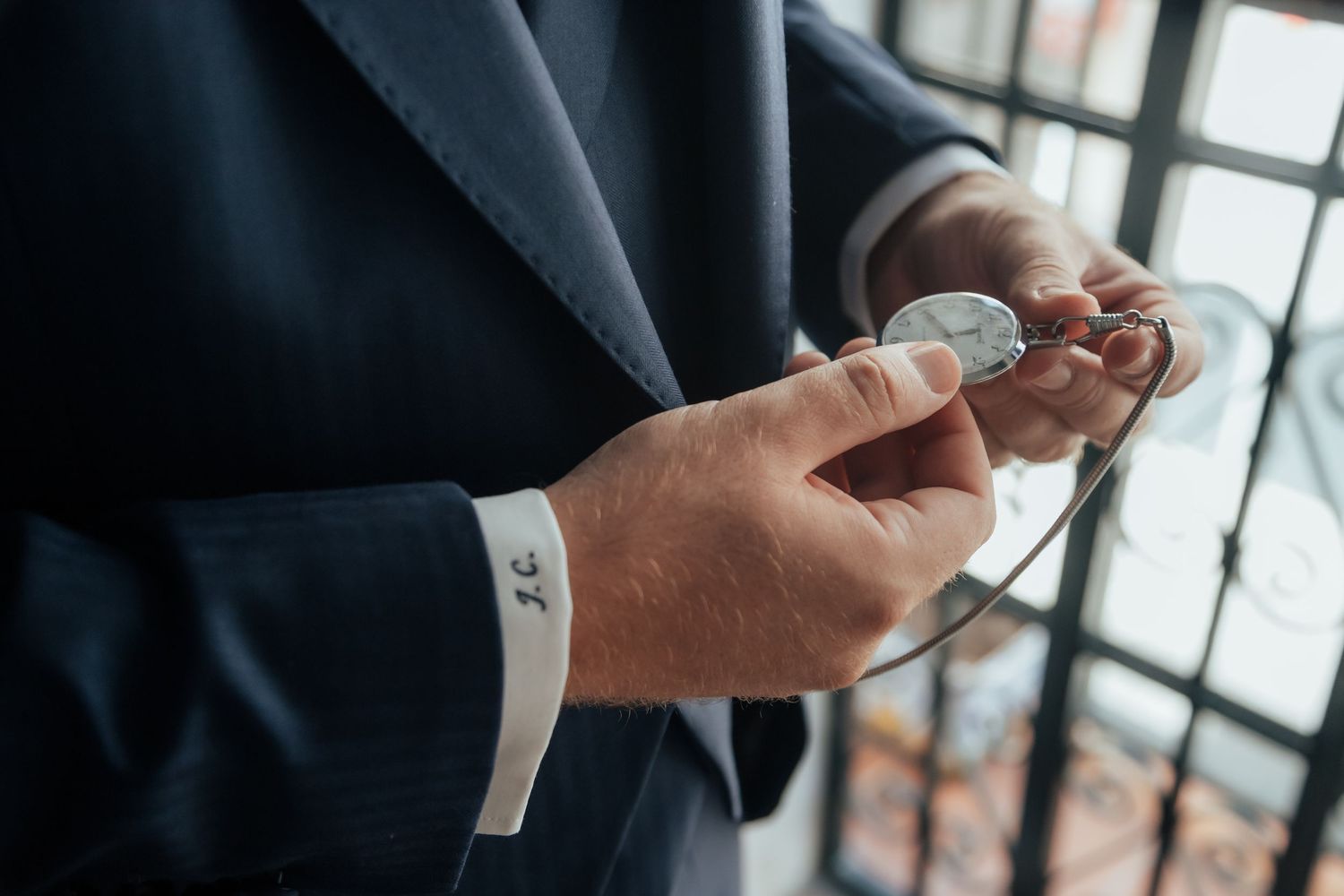 Close-up of groom fastening cufflinks on white dress shirt with navy suit jacket.