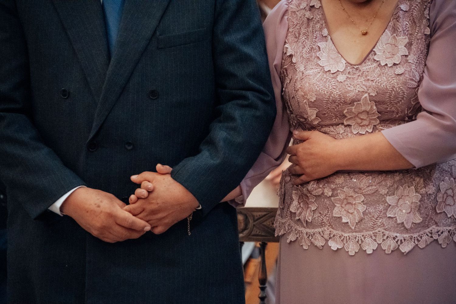 Close-up of couple holding hands during wedding ceremony, woman in lavender lace dress.