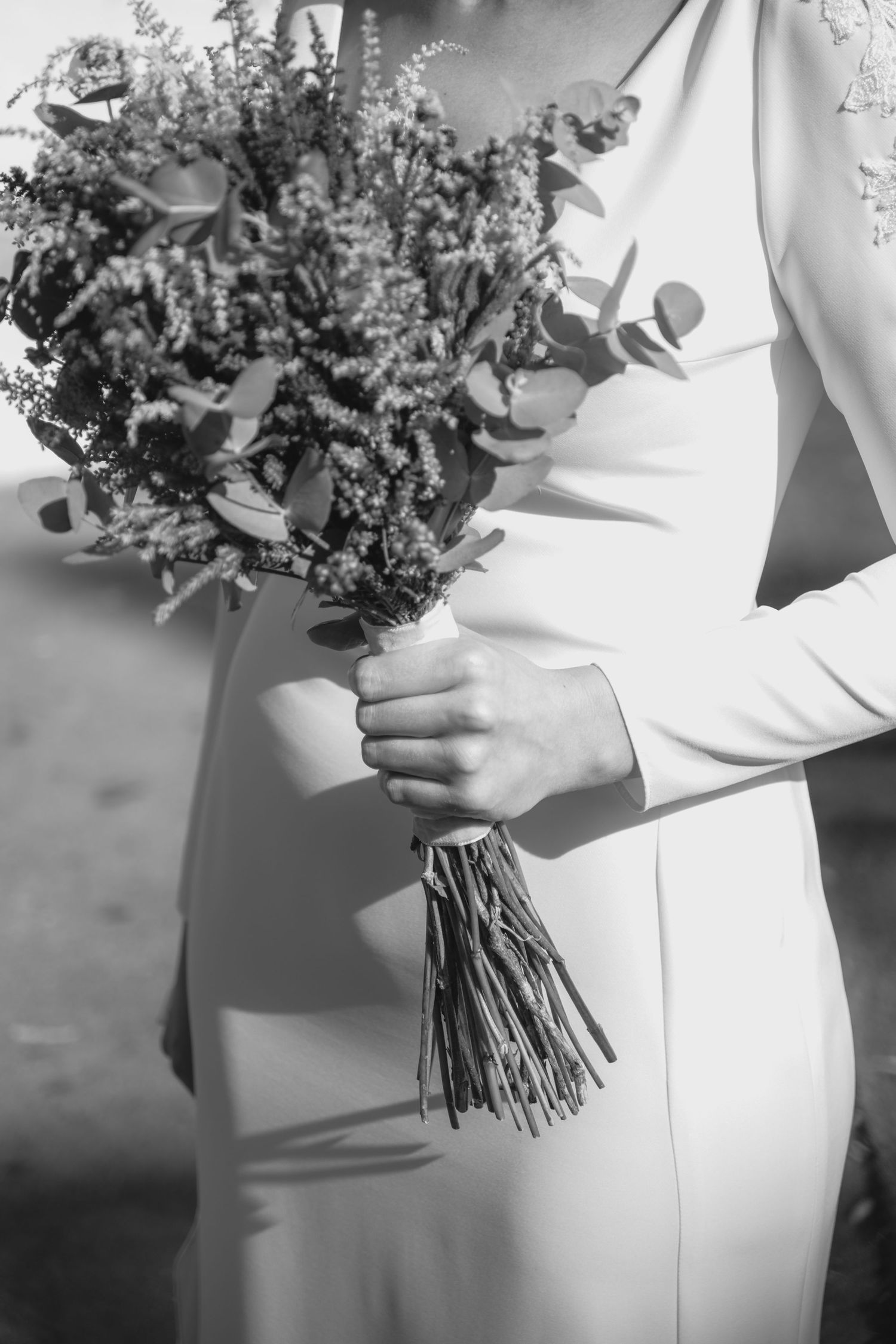 Black and white photo of a bride in a white gown holding a rustic wildflower wedding bouquet.