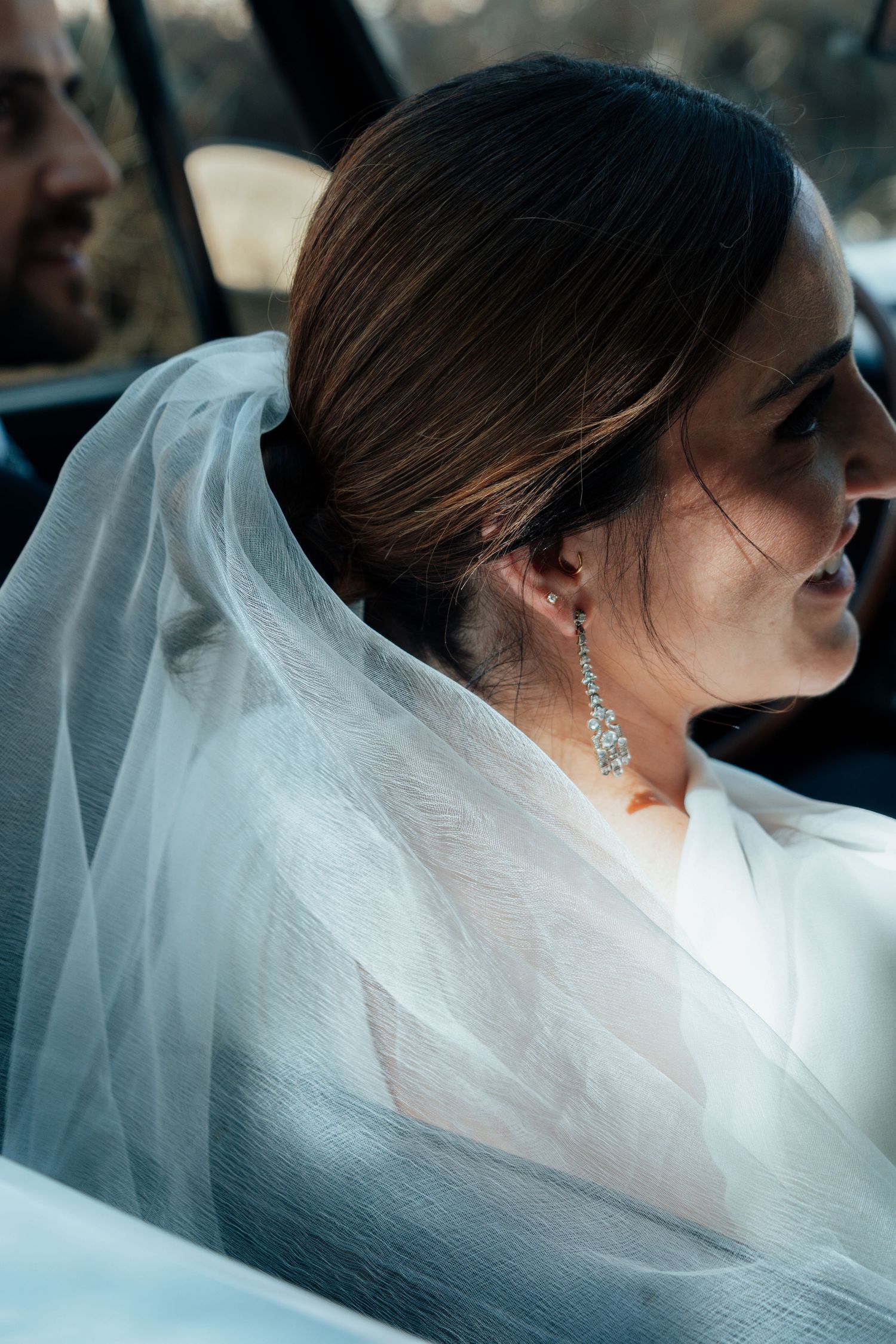 Close-up portrait of a bride wearing a veil and diamond drop earrings sitting in a vintage car.
