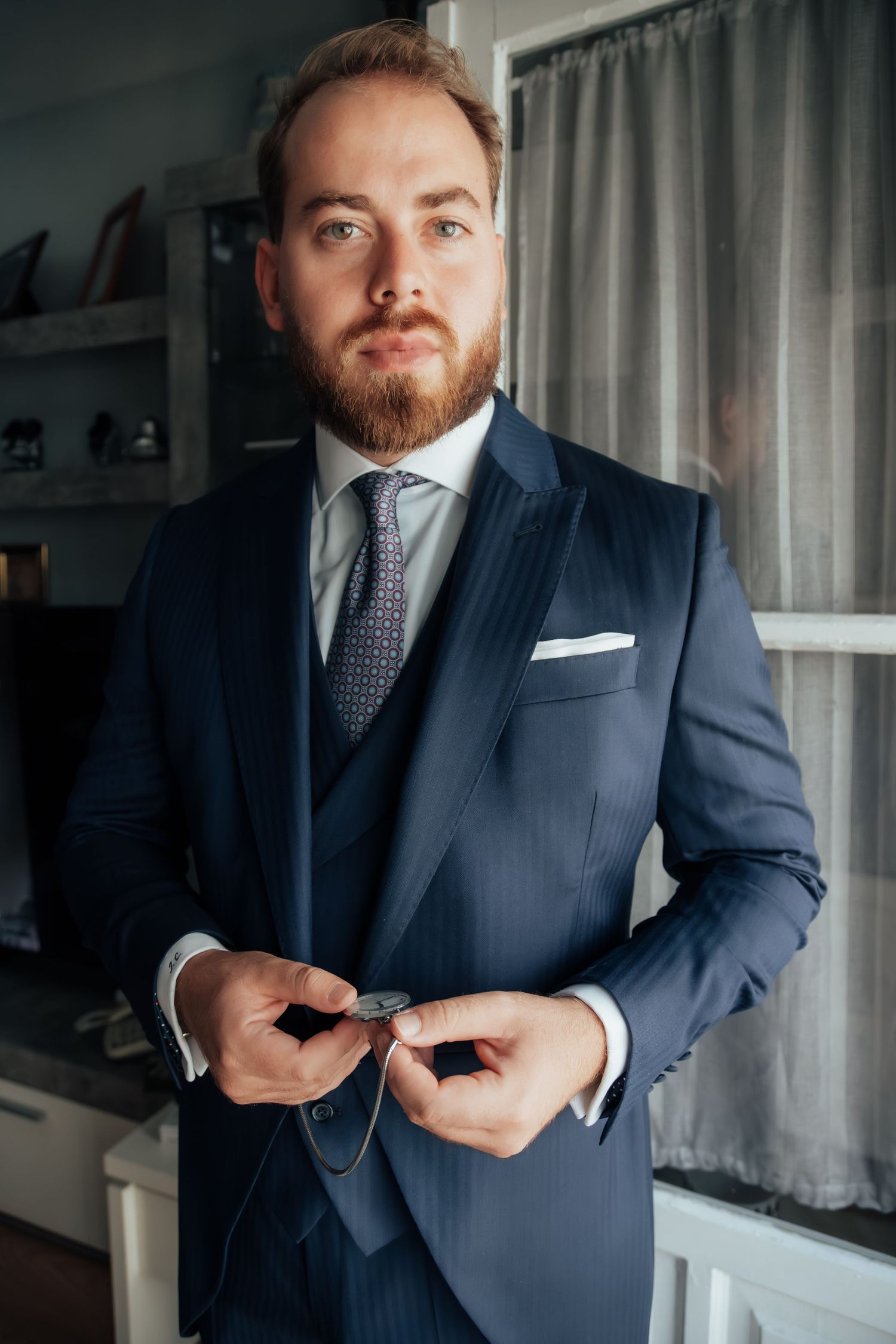 Dapper groom in navy three-piece suit adjusting cufflinks before wedding ceremony.