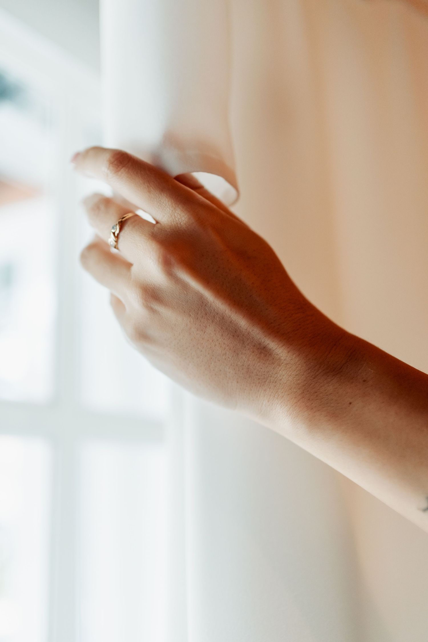 Close-up of bride's hand with gold engagement ring gently touching white wedding dress.